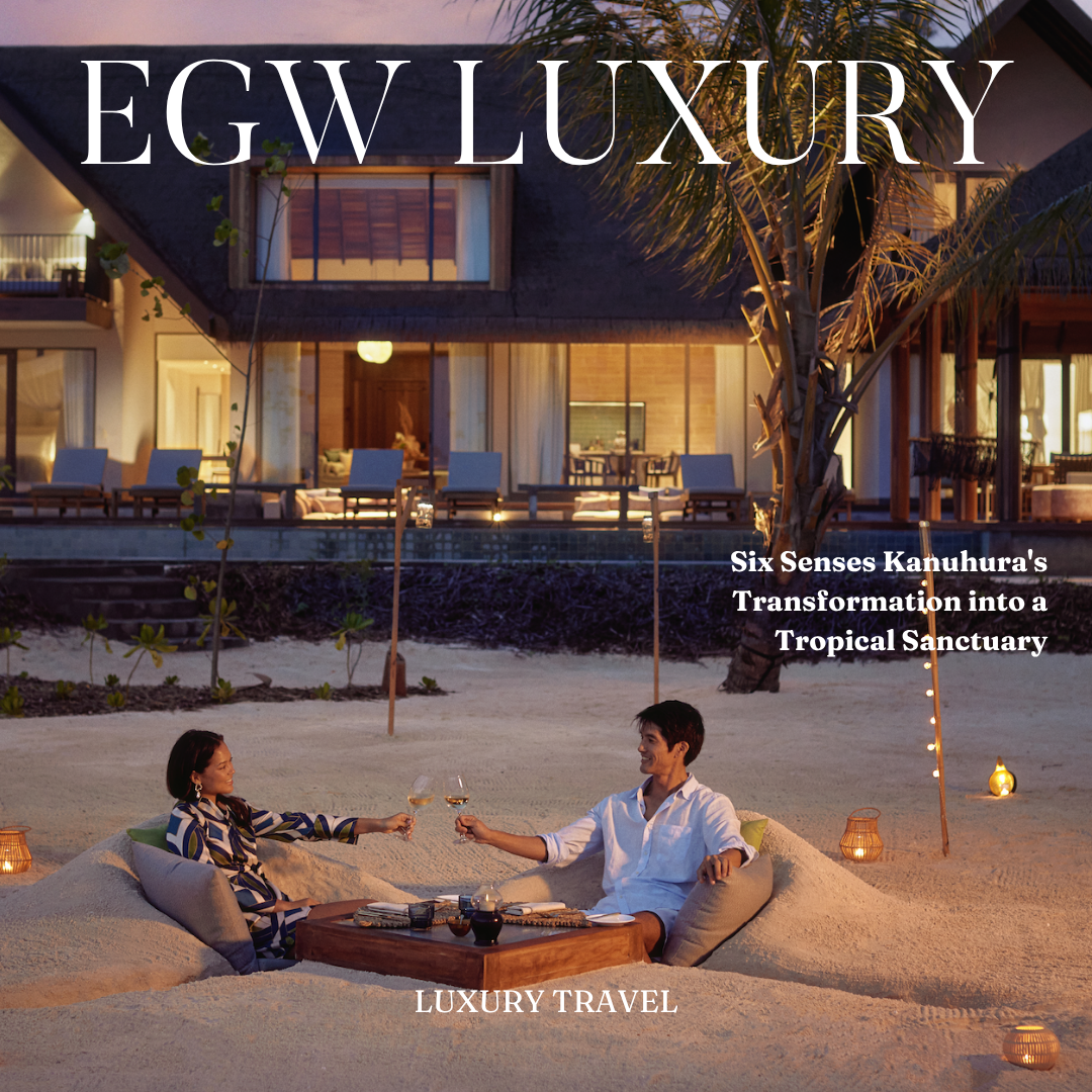 A tropical resort with a modern house, outdoor seating, and a sandy beach. Two people sit in a sandpit, toasting with glasses of wine, surrounded by lanterns at dusk.