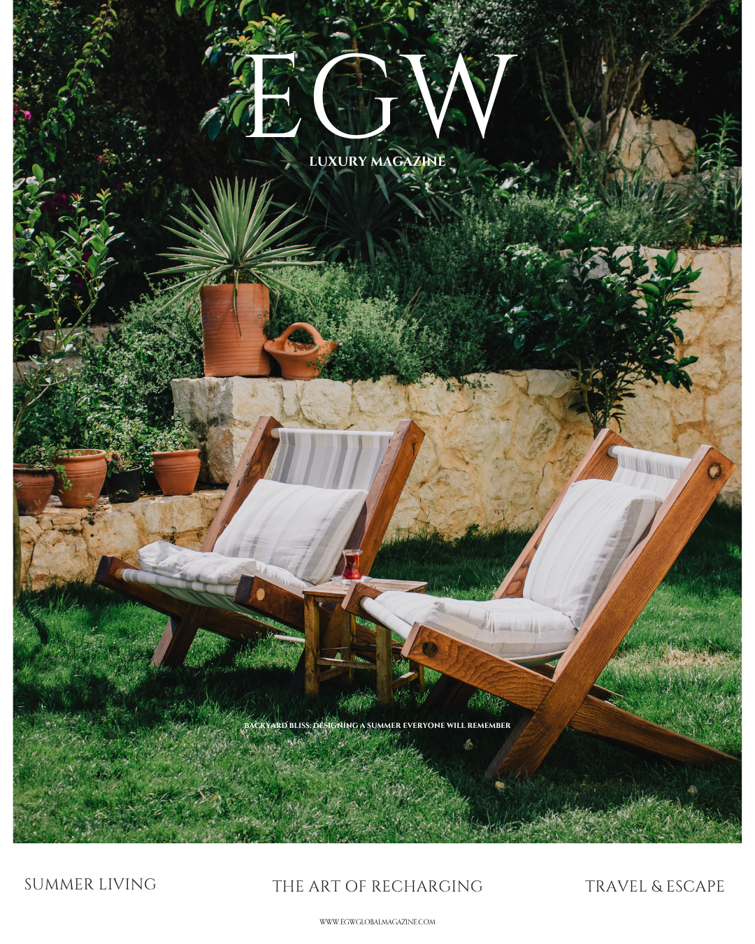 Cover of EGW luxury magazine featuring a garden scene with two wooden lounge chairs with striped cushions on green grass, potted plants, and a stone wall with various plants behind.
