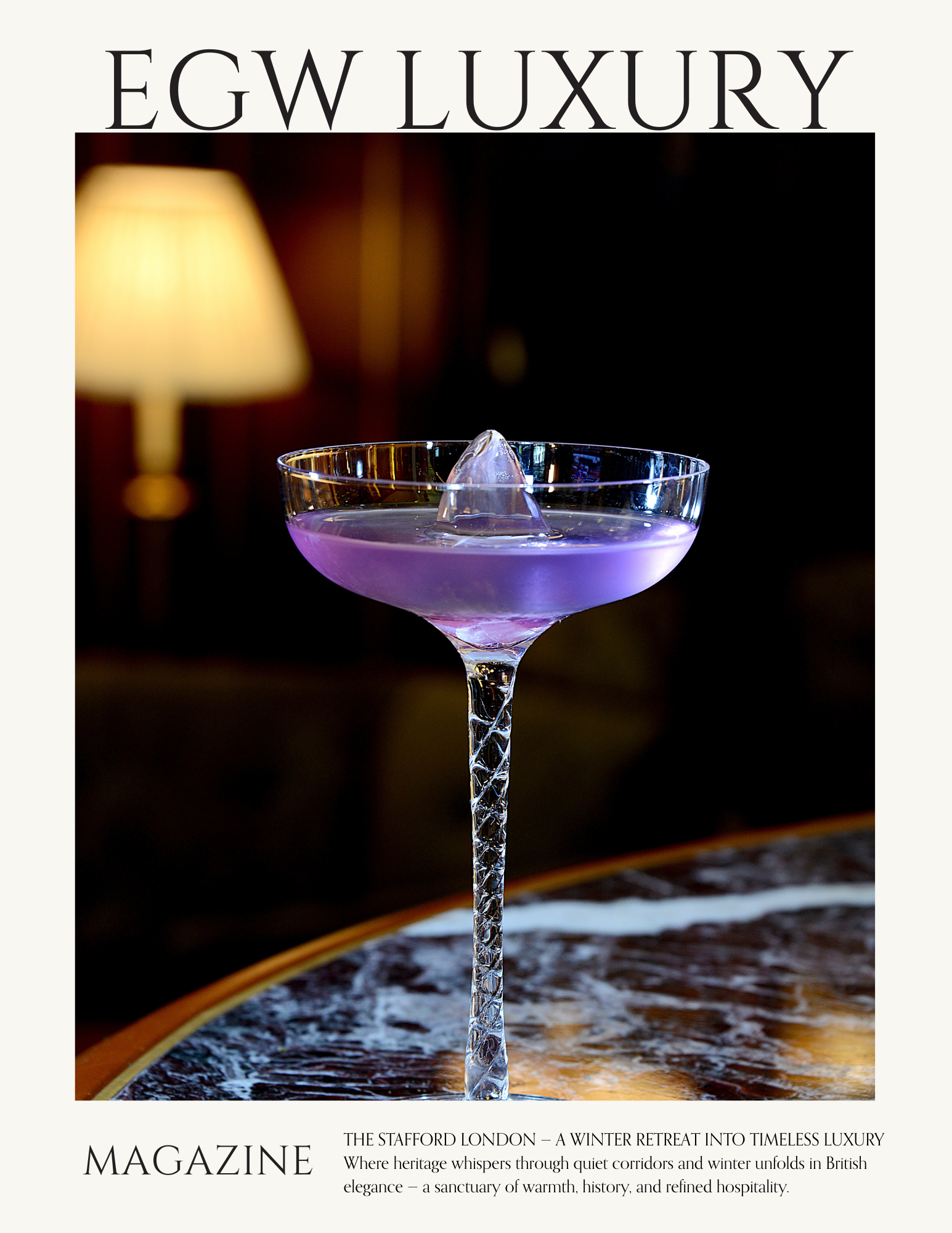 Close-up of a pink cocktail in a martini glass with a large ice cube, set on a dark wooden table with a blurred background featuring a lit lamp.