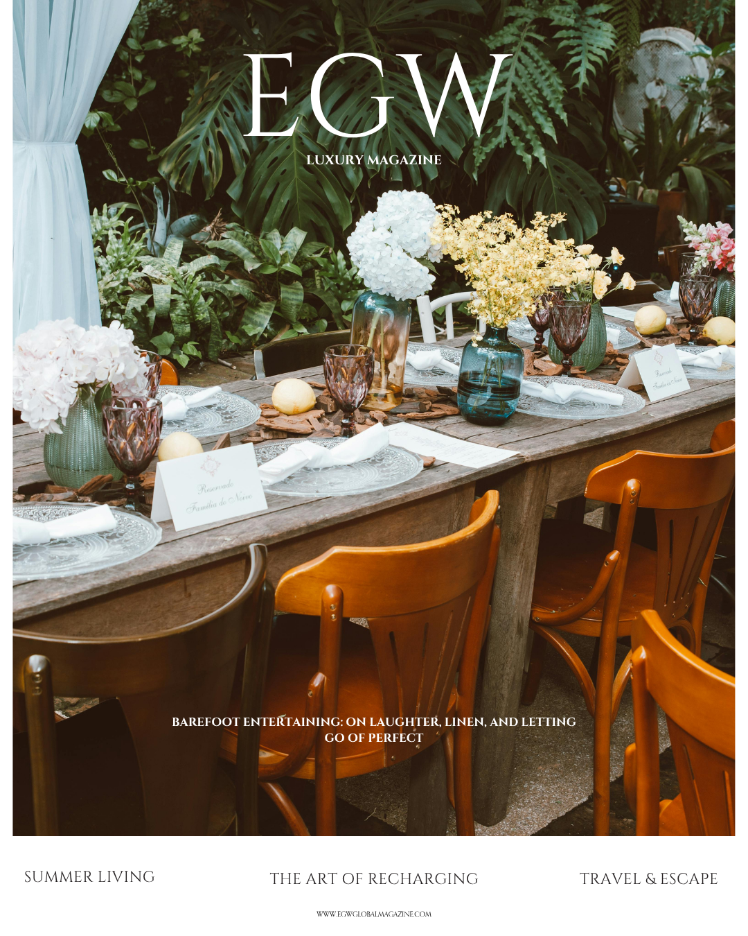 A beautifully set outdoor dining table with floral arrangements, glassware, and place cards, surrounded by lush green plants.