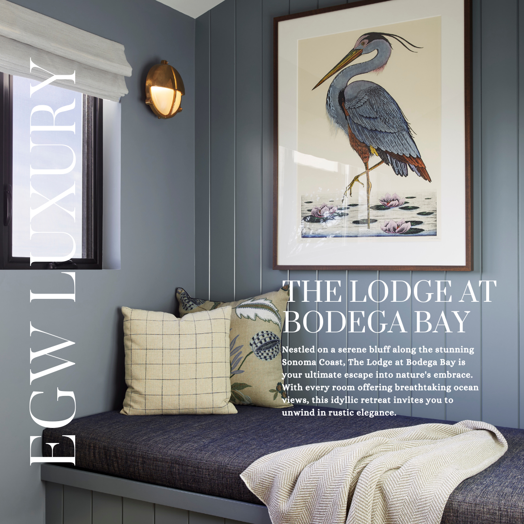 Interior of a cozy room with a blue wall, a window with a white blind, a brass wall sconce, a bed with plaid and floral pillows, a beige blanket, and a large framed painting of a heron standing on water lilies.