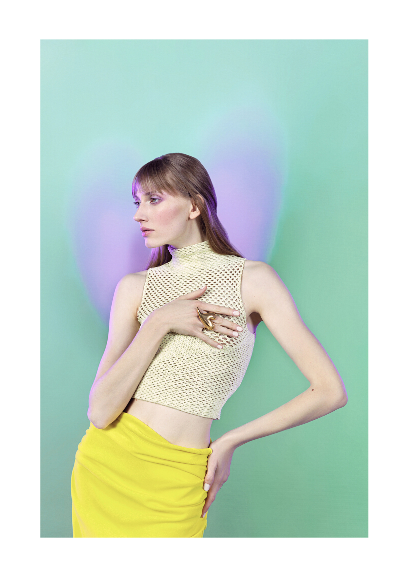 A woman with light skin and straight brown hair styled with bangs, wearing a sleeveless yellow skirt and a beige textured crop top, stands against a pastel green background with purple and blue lighting effects. She poses with her left hand on her wa