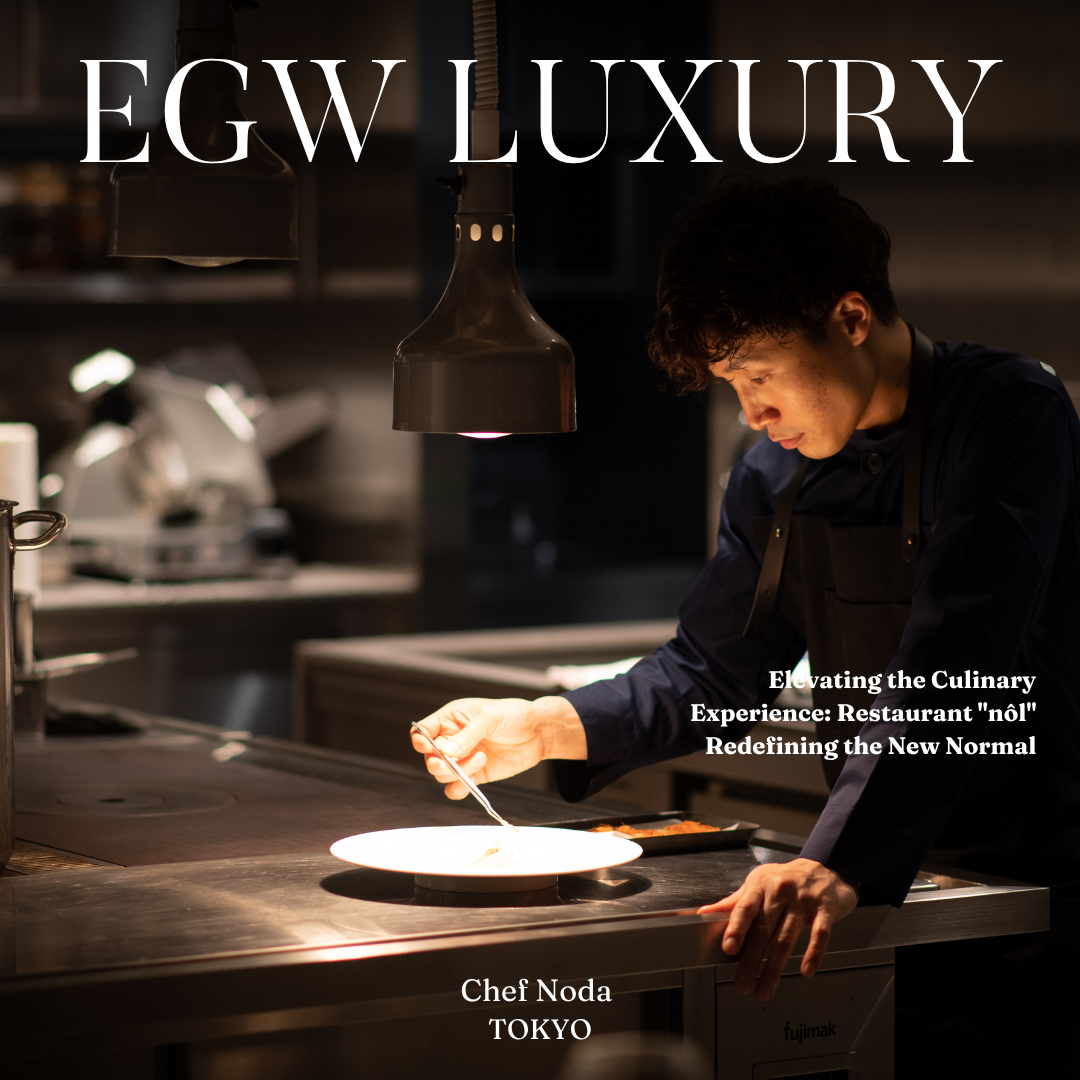 A chef preparing food in a professional kitchen under a black lamp with the words "EGW LUXURY" on the top. The chef is focused on plating, with kitchen equipment in the background.