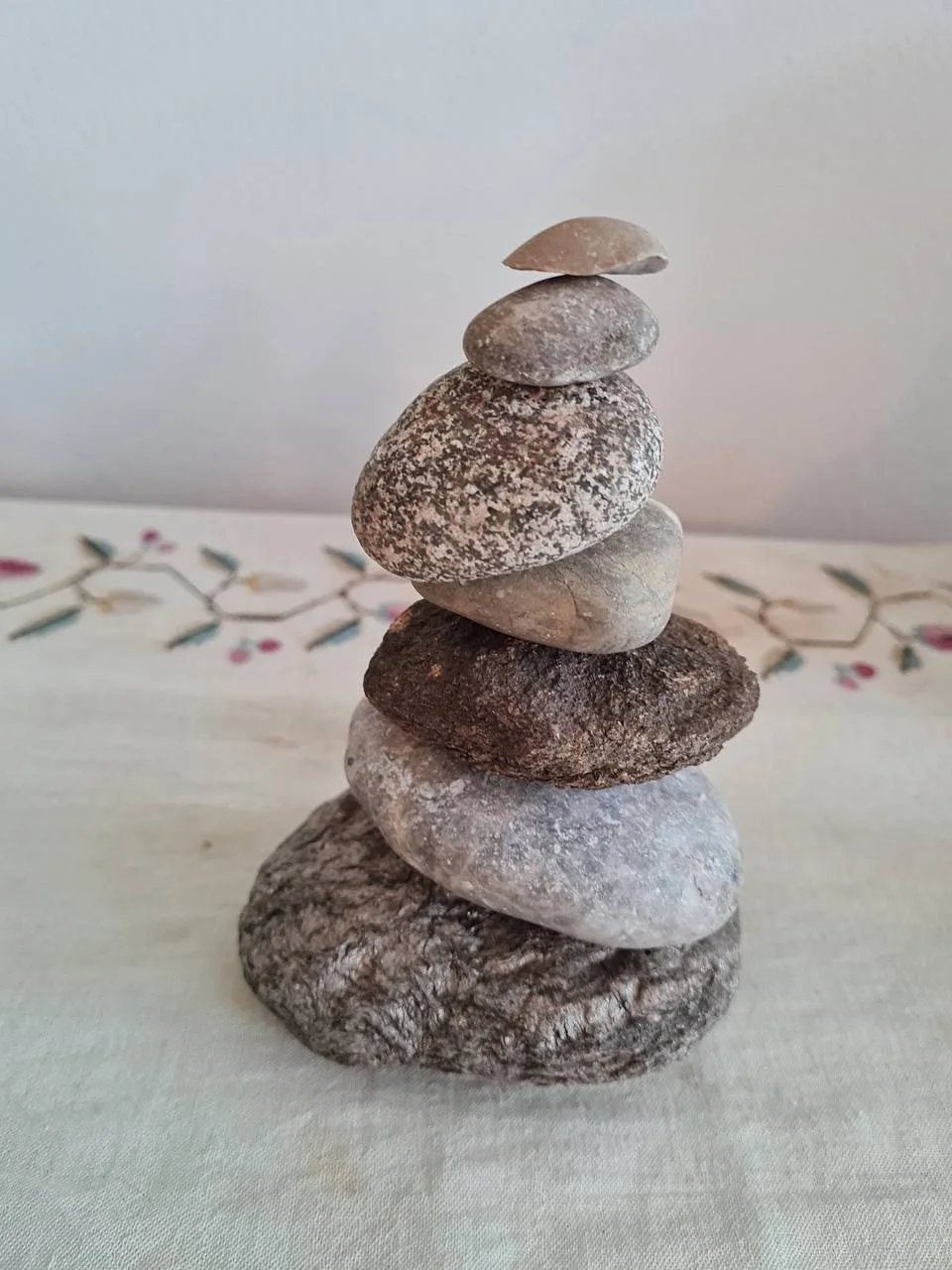 Gestapelte Steine in verschiedenen Größen und Farben auf einem Tisch mit dekorativem Tuch im Hintergrund.