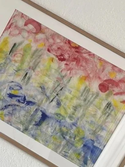 Abstraktes Wasserfarbenkunstwerk mit roten, gelben, grünen, blauen und violetten Farbflächen, in einem Holzrahmen an der Wand aufgehängt.