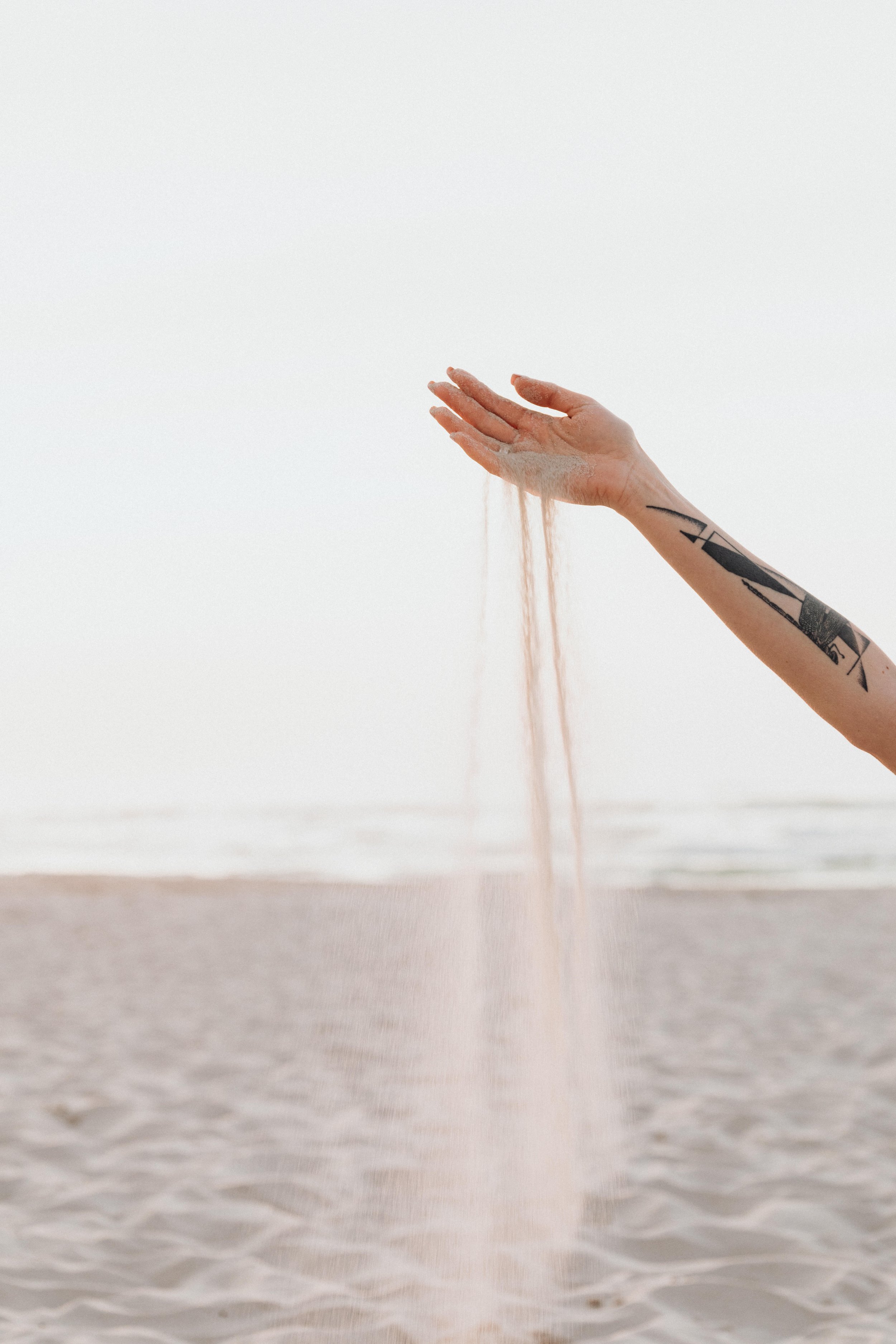 Person's hand with tattoos holding sand, underwater at the beach.