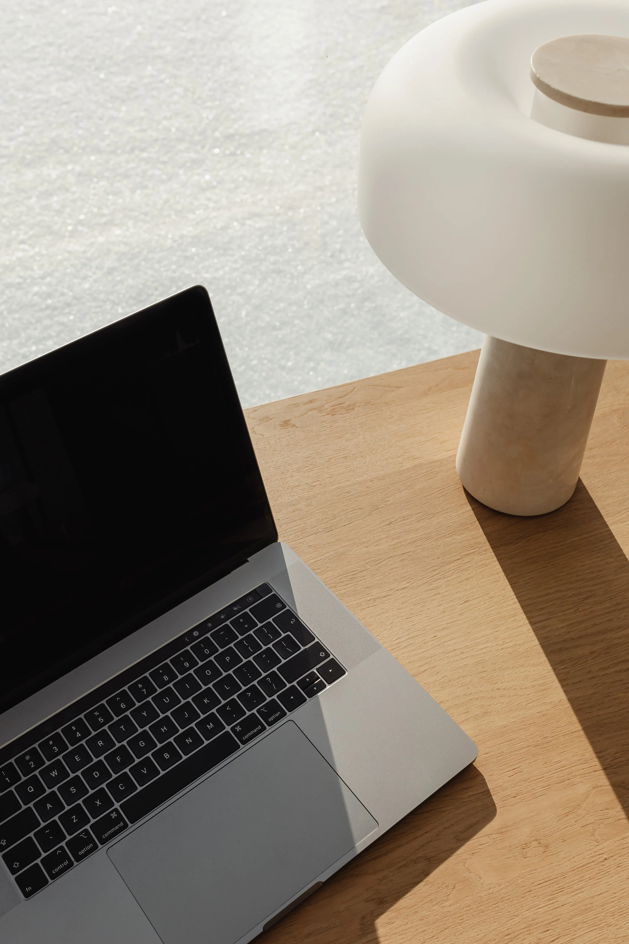 Laptop on a wooden table with a black screen, a white modern lamp, and a ceramic cup in the background.