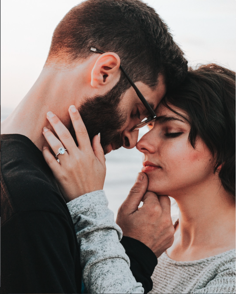 A close-up of a young couple with their foreheads and noses touching, sharing an intimate moment outdoors.