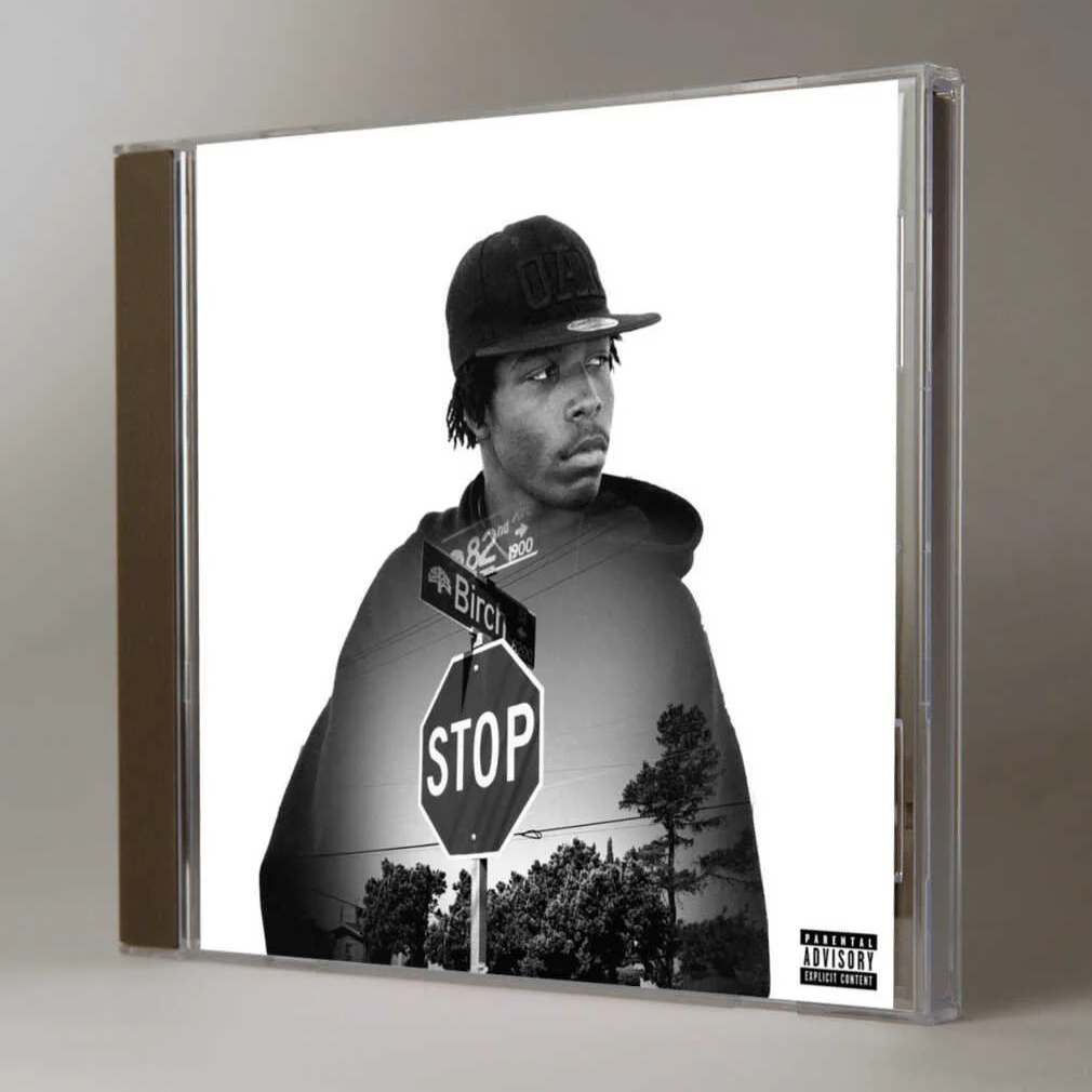 Black and white album cover featuring a young man wearing a baseball cap, with a stop sign, street signs, and trees in the background.