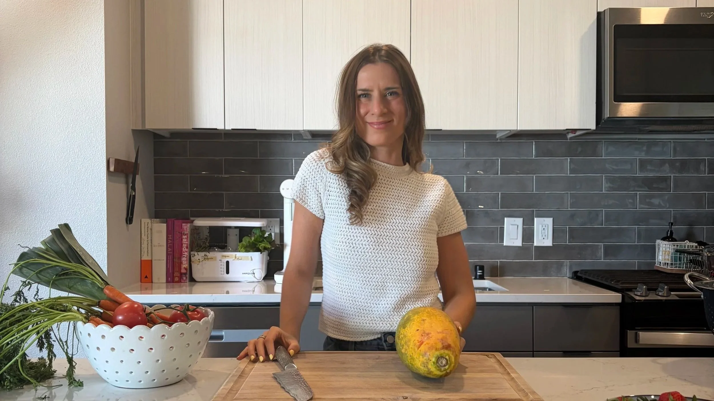 Dietitian las vegas standing in a modern kitchen, holding a large yellow and green gourd on a wooden cutting board, with a chef's knife nearby.