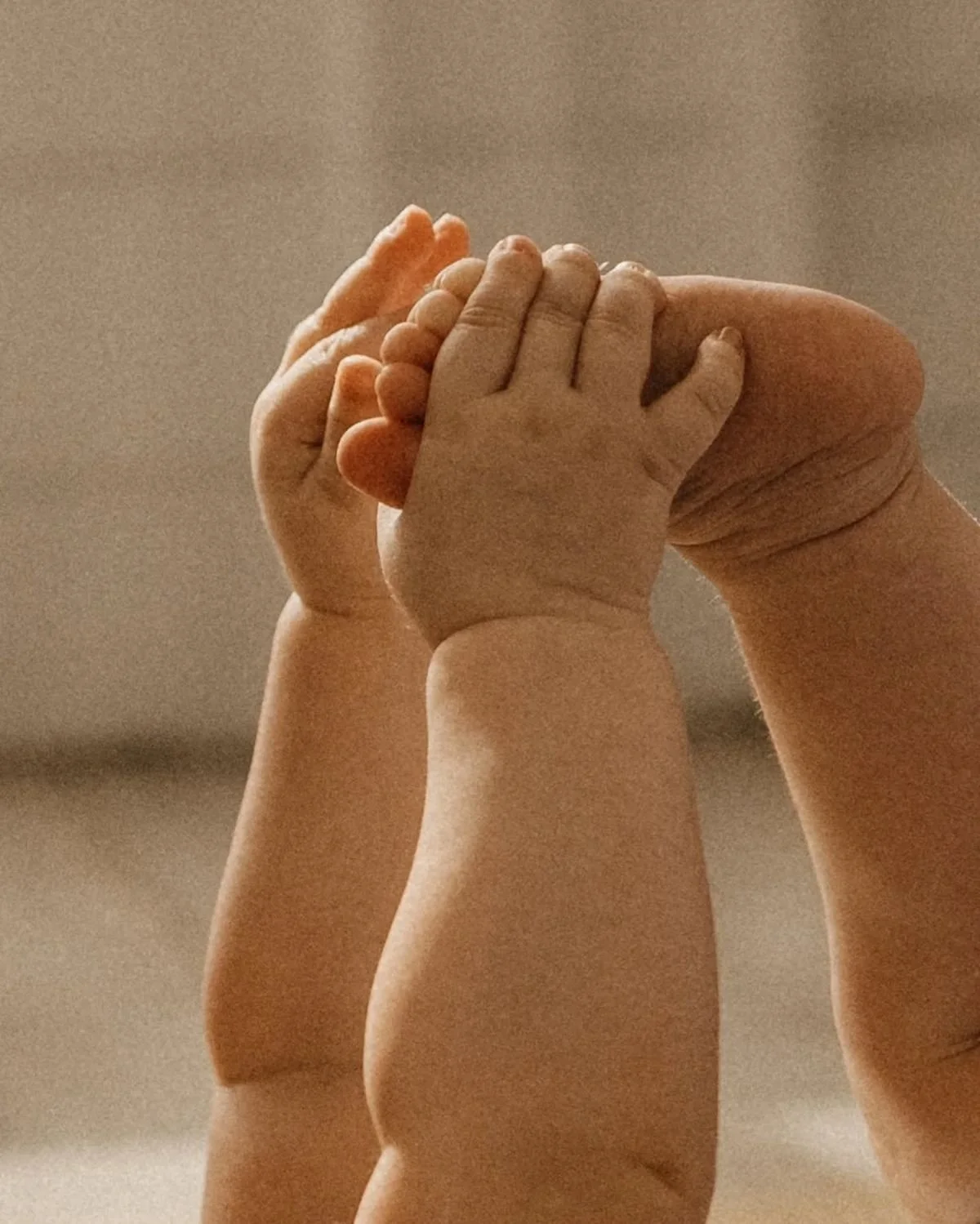 Close-up of a child's hand grasping an adult's finger, with a neutral background.