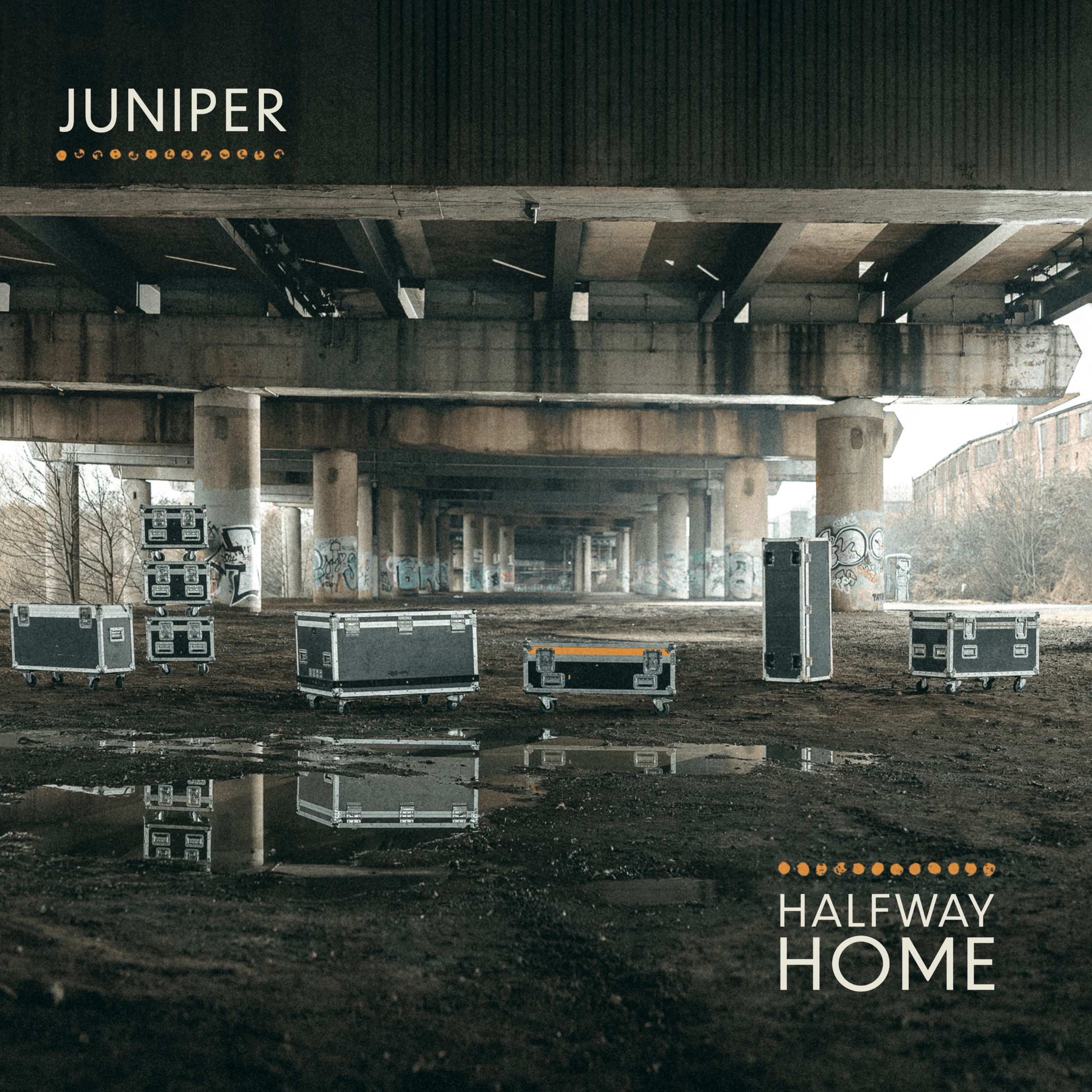 Album cover for Halfway Home. Underneath a highway overpass with pillars, there are multiple large black flight cases on wheels. Text on the top left reads 'JUNIPER' with orange dot accents, and text on the bottom right reads 'HALFWAY HOME'.