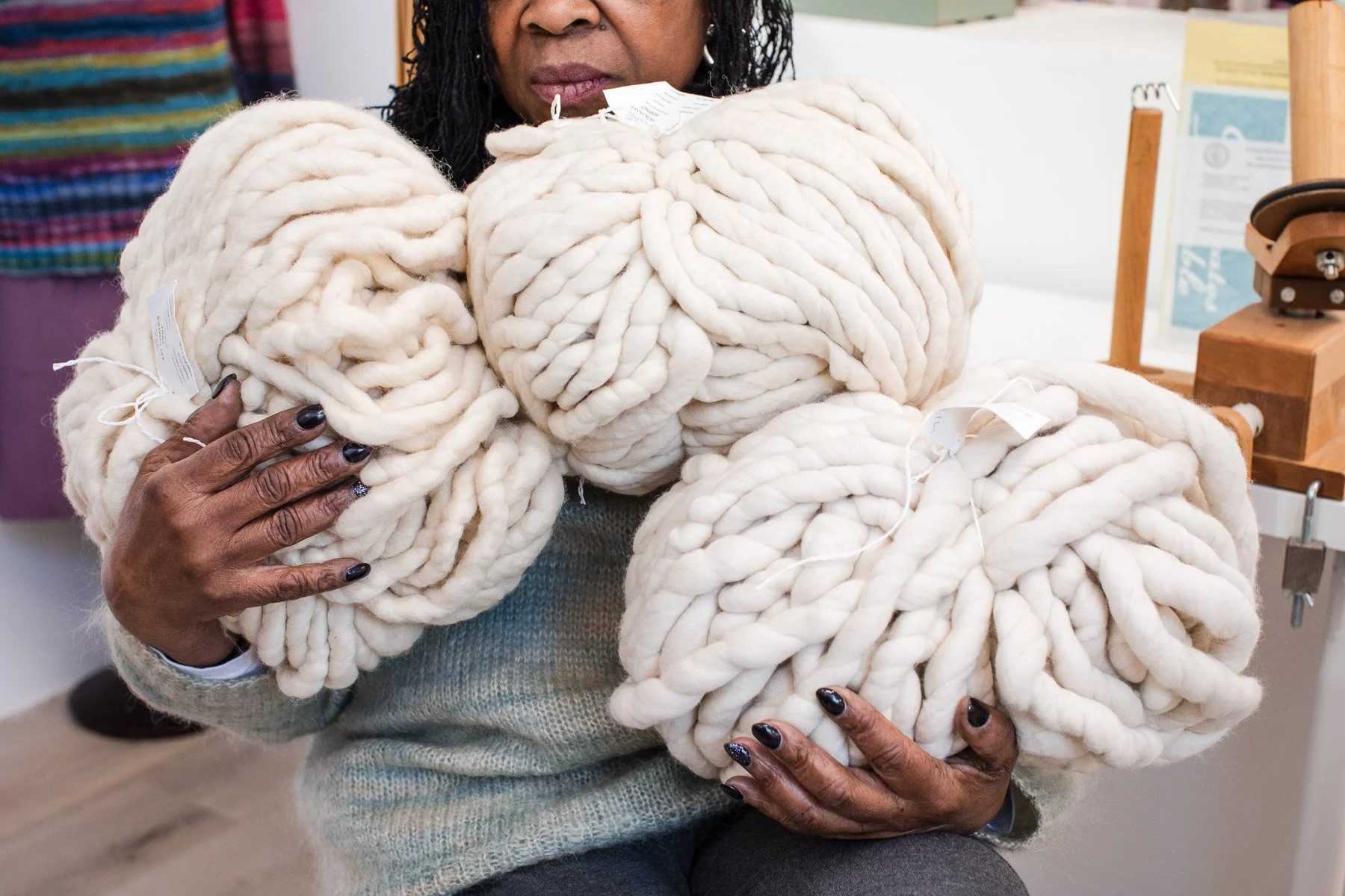 A woman holding several large, thick, white knitted yarn balls in a store or craft shop.