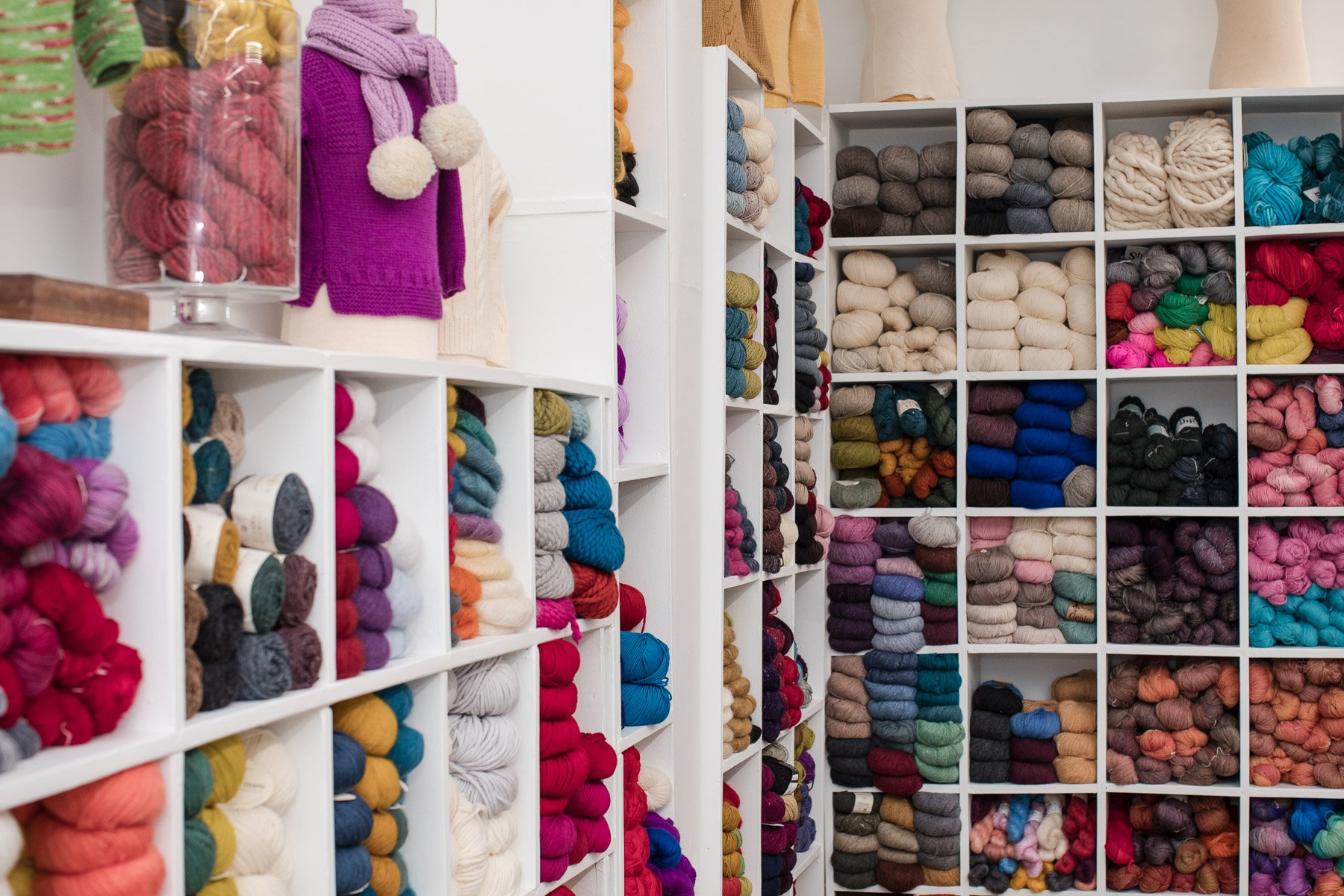 Shelves filled with neatly organized balls of colorful yarn in a craft store or knitting shop.