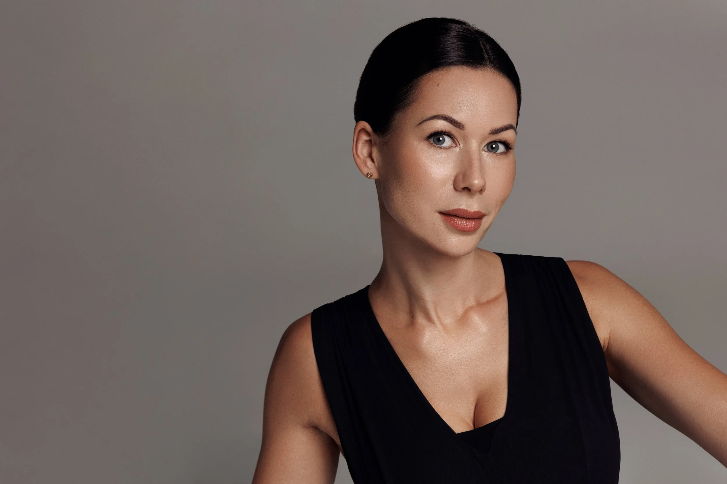 Ketija, wearing a black sleeveless top, poses against a plain grey background.