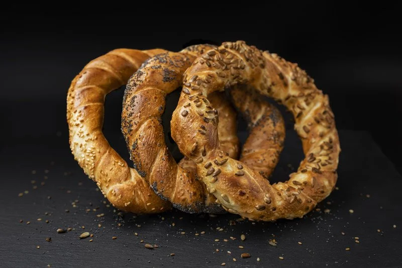 Trei covrigei cu diferite garnituri, așezați pe o suprafață neagră, pe un fundal negru.