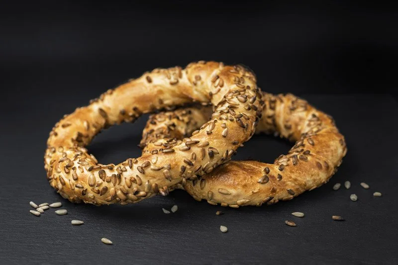 Două bagele cu semințe de susan și semințe de floarea-soarelui, așezate pe o suprafață de culoare închisă.