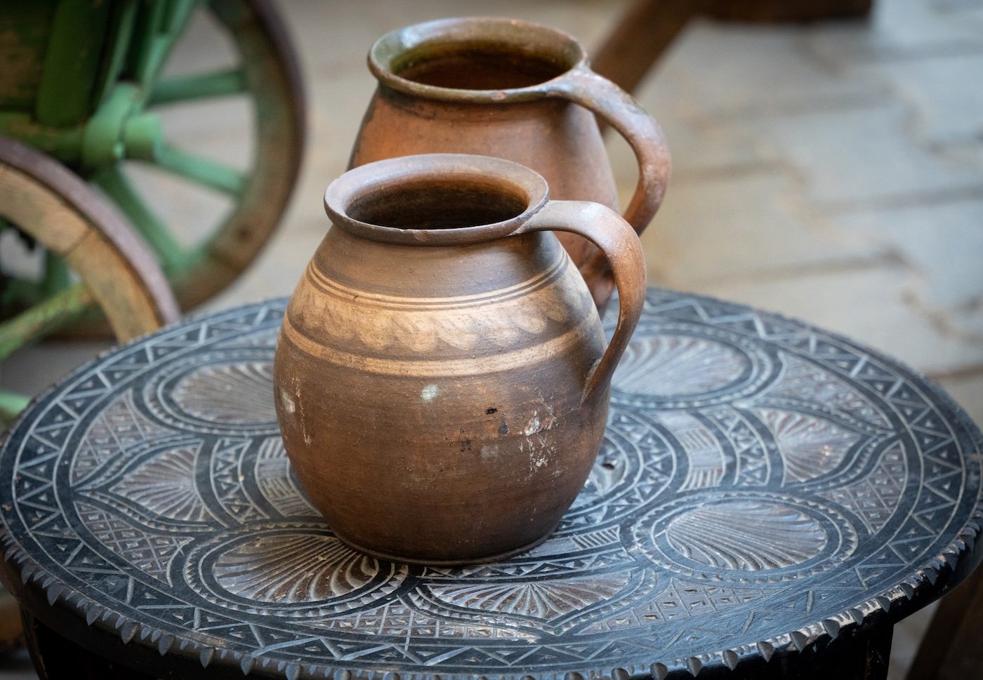 Două căni rustice din lut, pline cu apa, așezate pe o masă decorativă din metal negru.