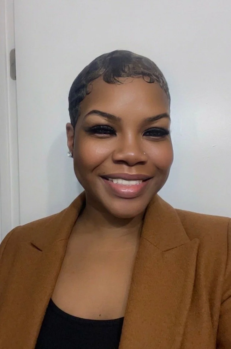 A smiling woman with short, dark hair wearing a brown blazer and black top.