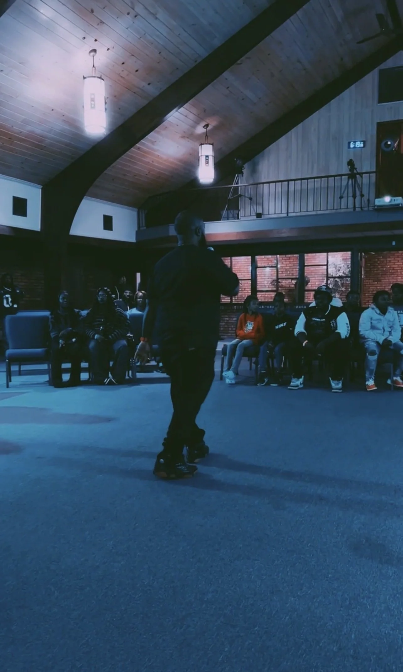 A person roller skating in an indoor space with an audience seated along the wall, some wearing face masks.