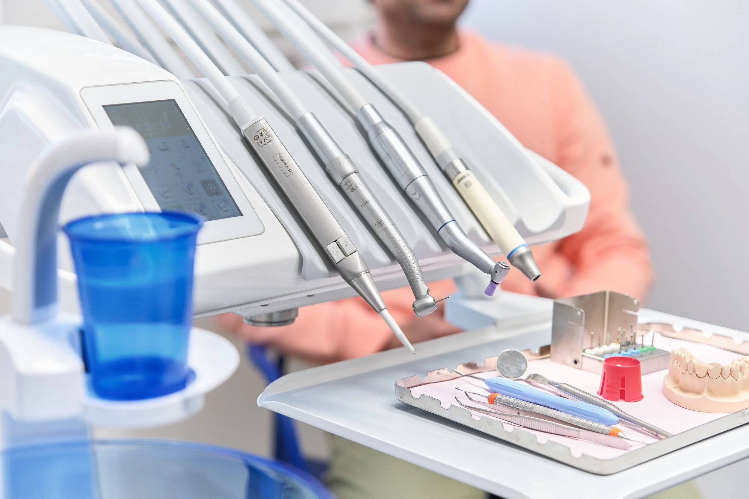 Närbild av tandläkarutrustning med handinstrument och en tandläkare i bakgrunden.