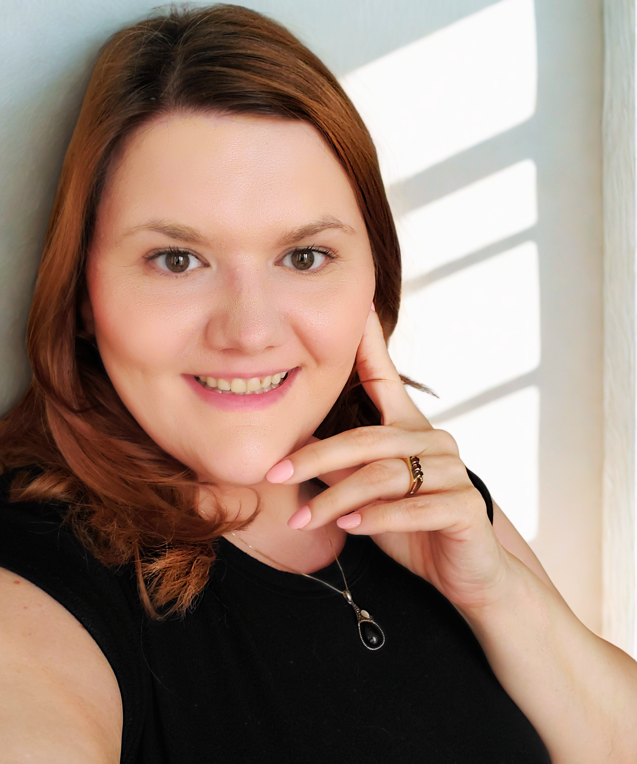 Image of the clinic owner. She is looking directly at the camera, with a gentle smile, and her pointer finger by her cheek and middle, ring, and baby finger by her chin.