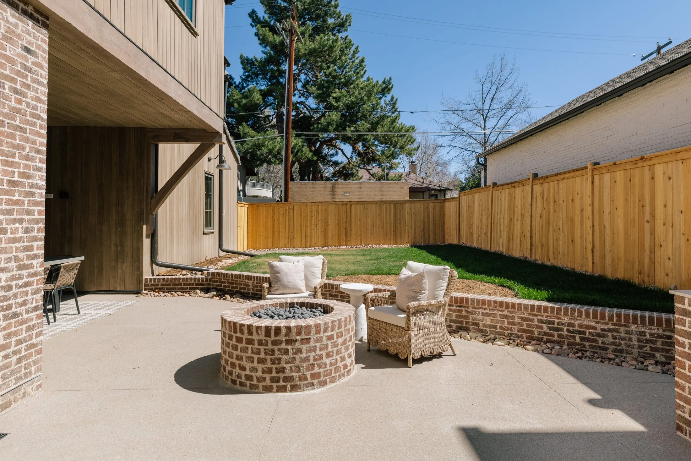 Backyard with a fire pit surrounded by chairs, green grass, and a wooden fence.