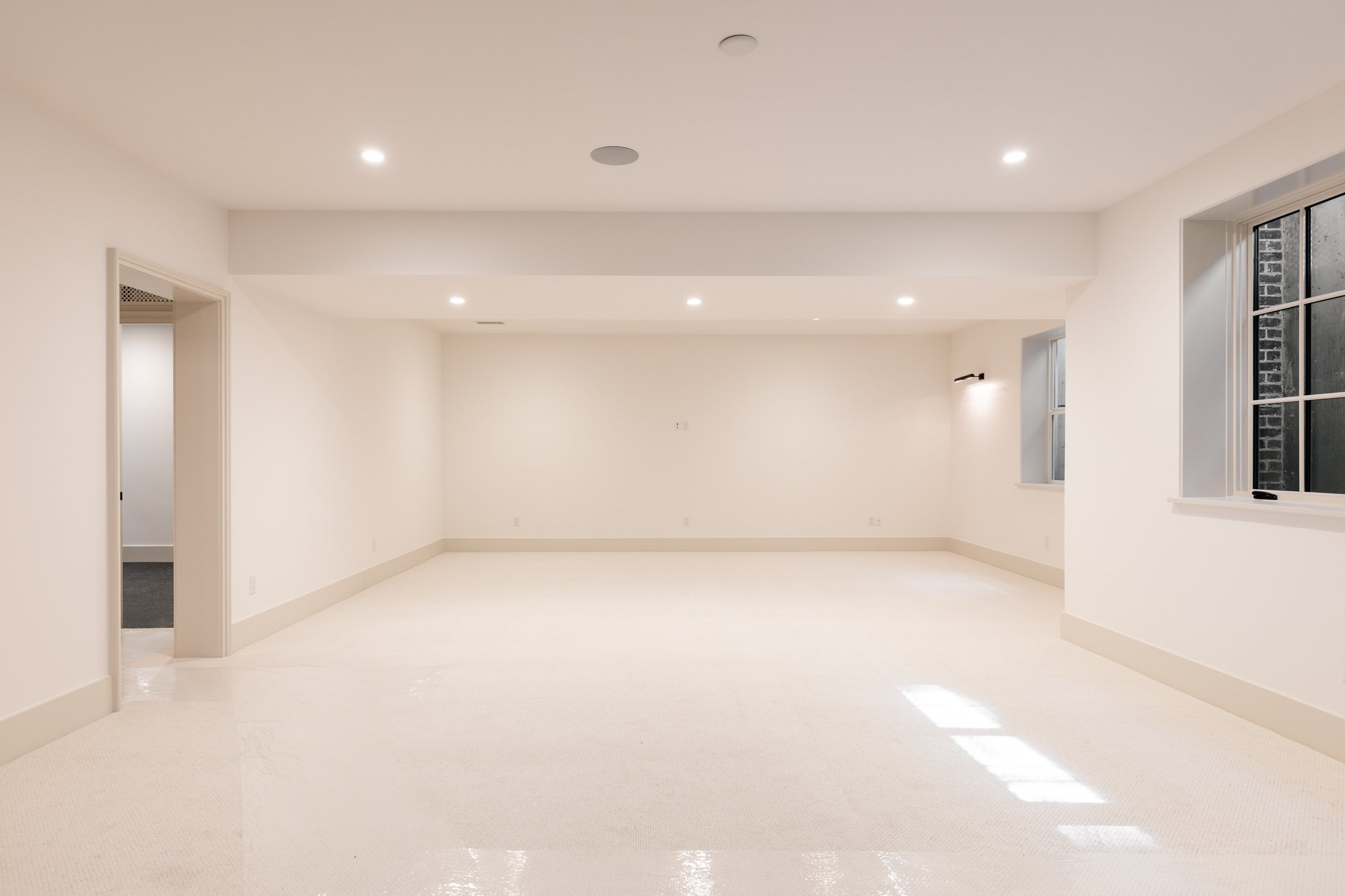Empty white room with large windows and recessed lighting.