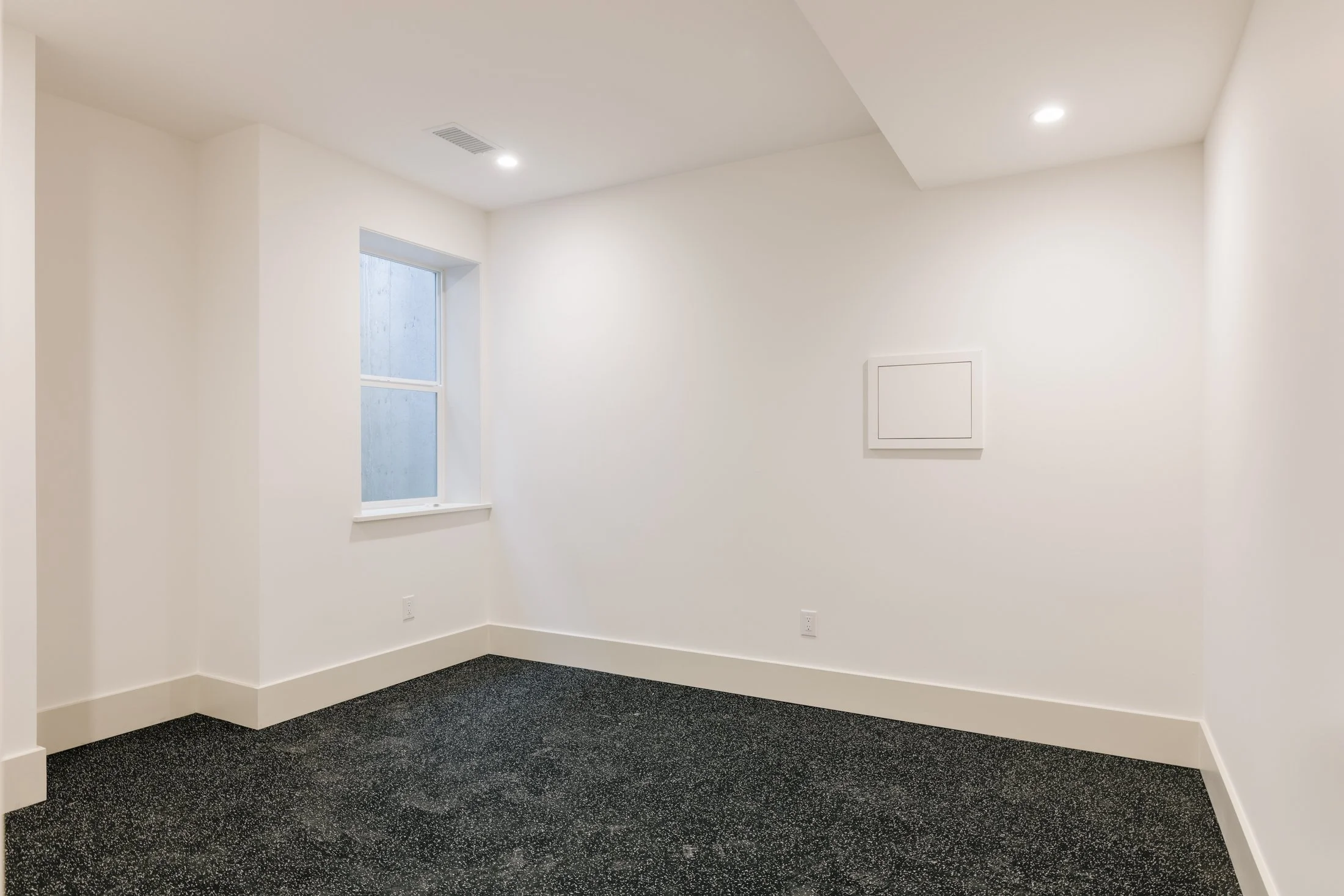 Empty white room with a window, carpet flooring, and ceiling lights.