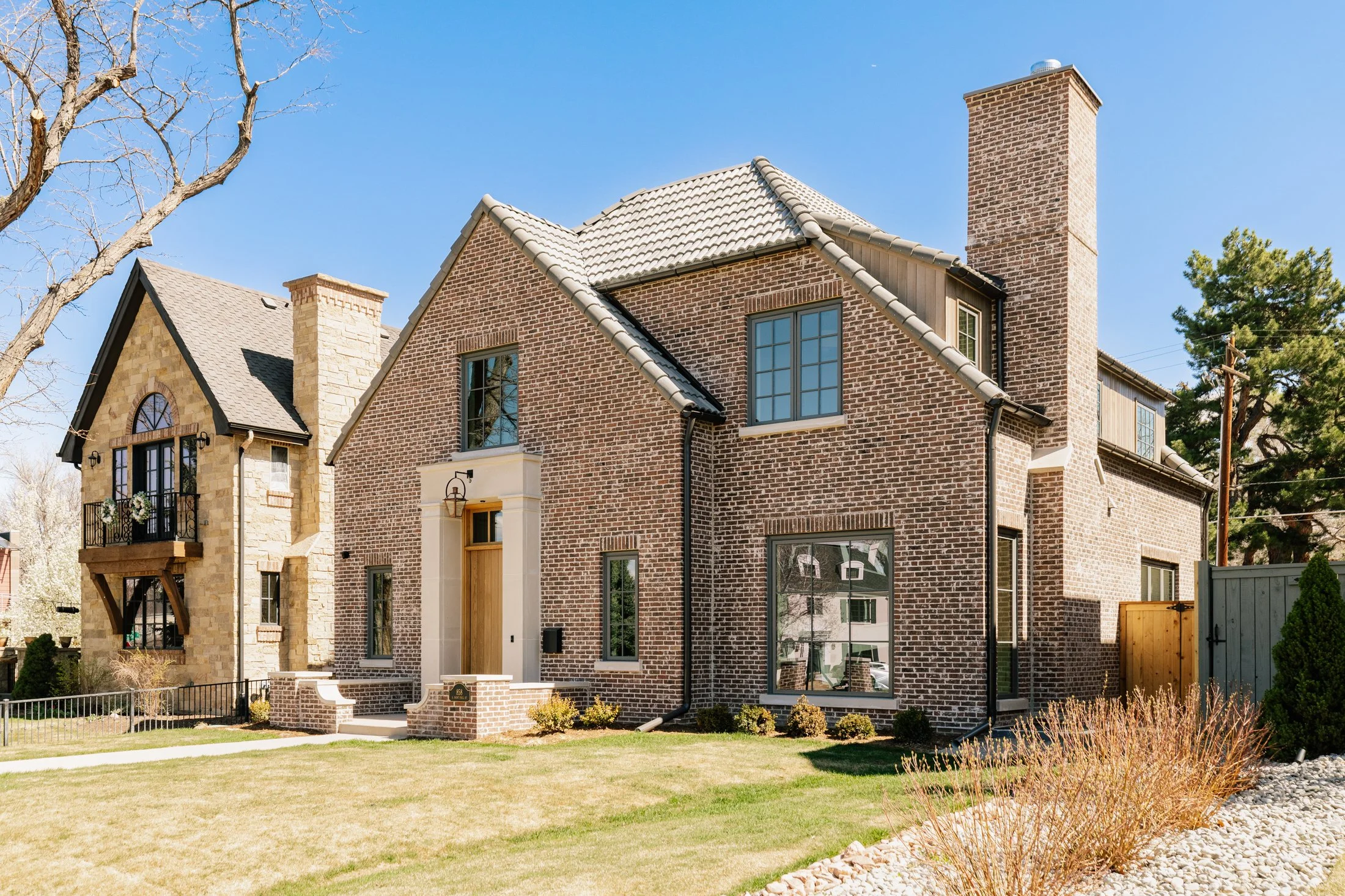 Front view of a brick house with a stone section, well-maintained lawn, and a clear blue sky.