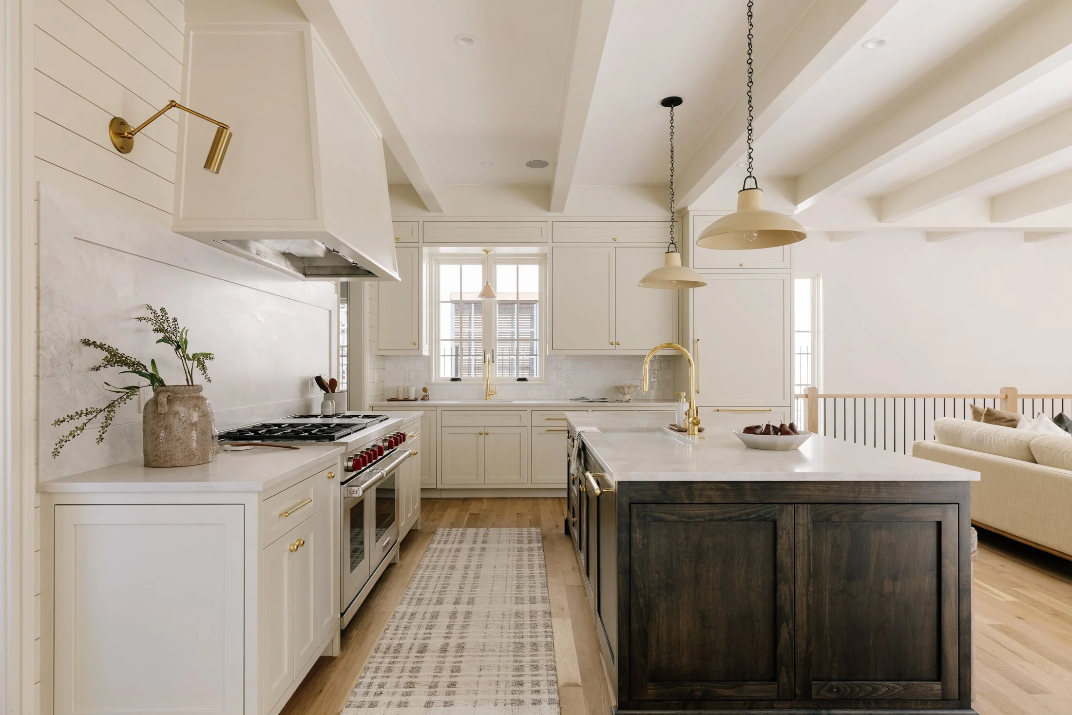 A modern kitchen with white cabinets, a black island, gold fixtures, and a beige sectional sofa visible in the background.