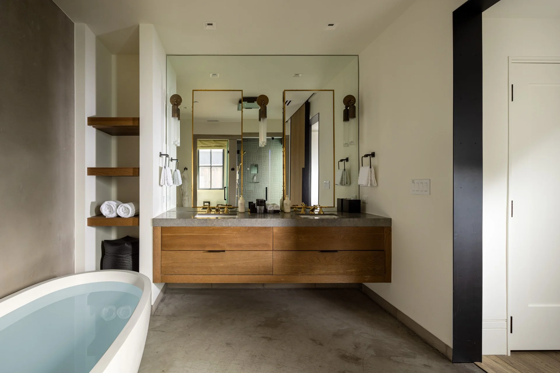 Modern bathroom with a double vanity, large mirror, and a bathtub on the left. White walls, wooden cabinetry, and a concrete floor.