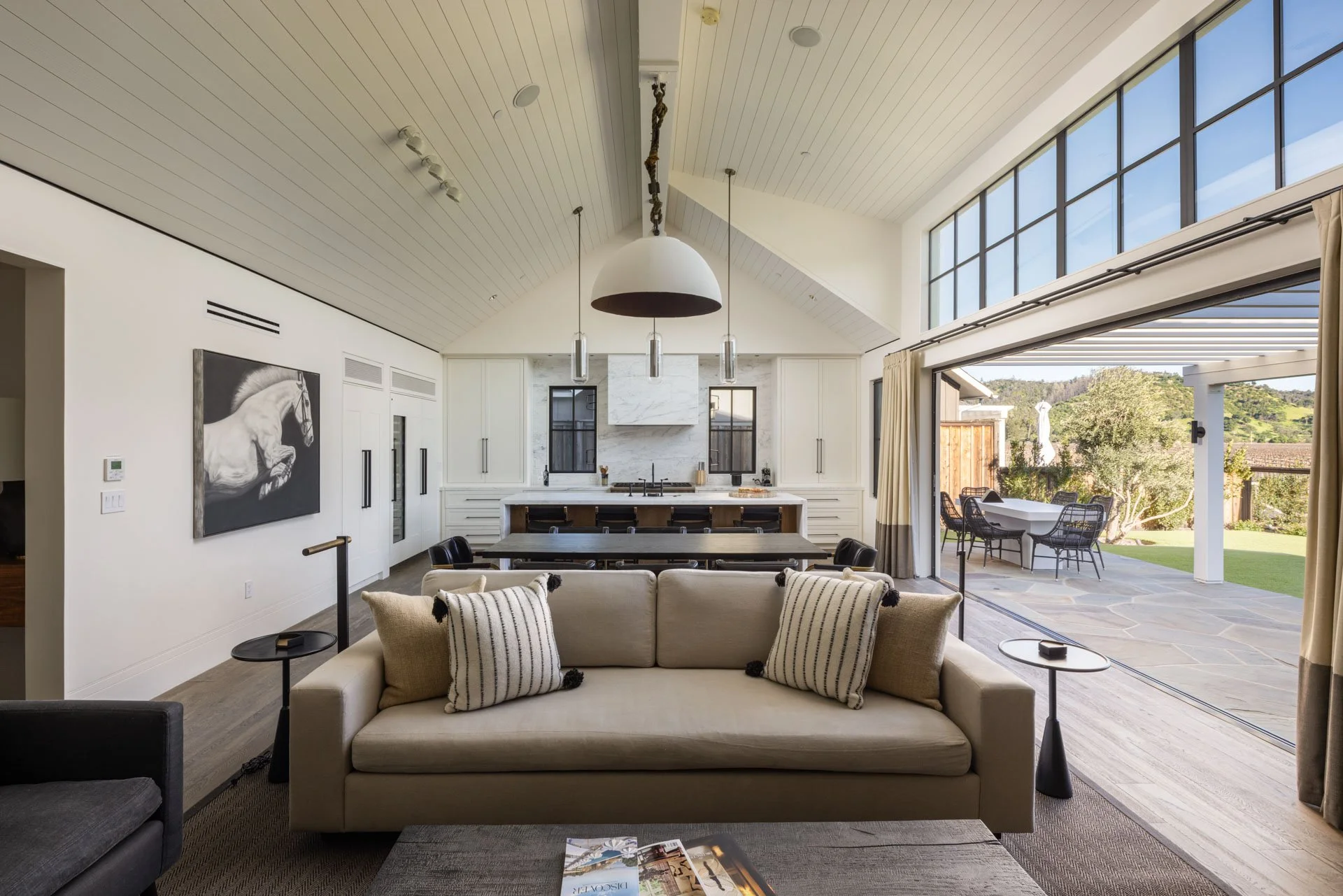 Open-concept living room with large sliding glass doors opening to outdoor patio, modern kitchen with white cabinetry, and seating area with beige sofa.