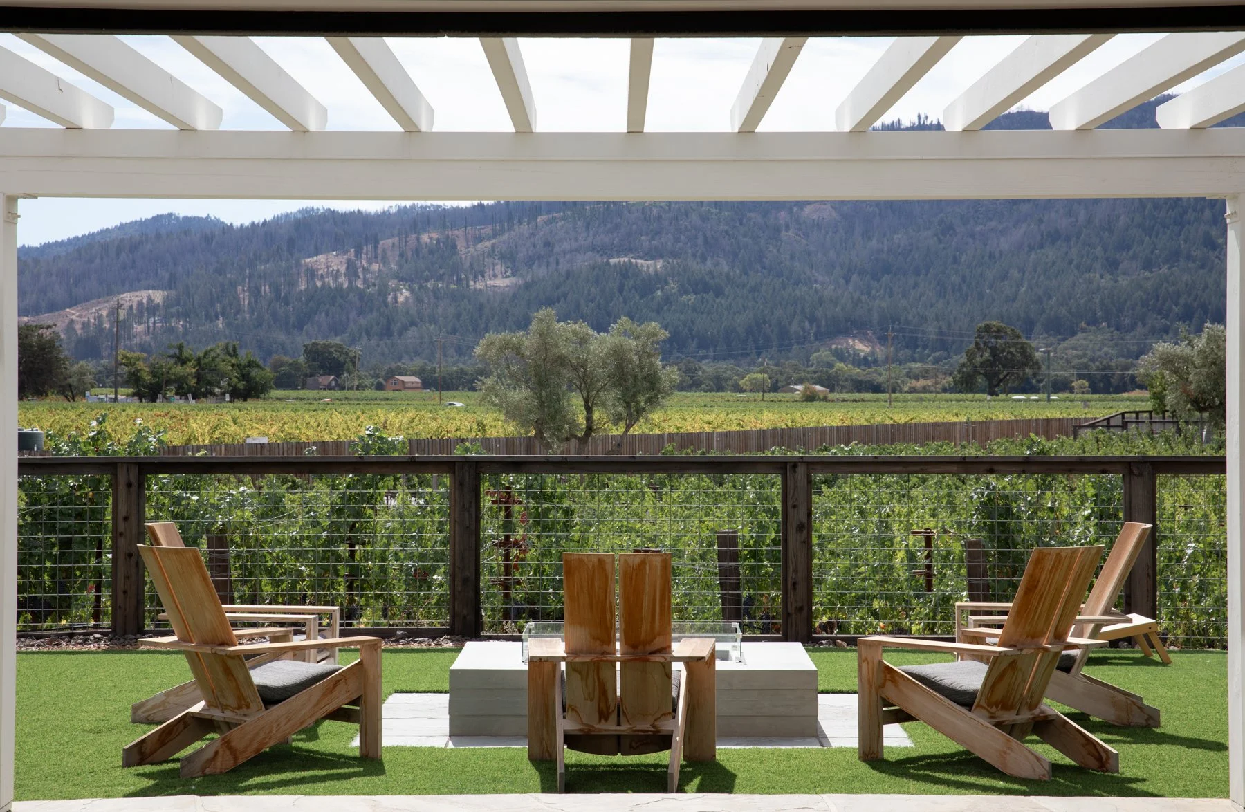 Outdoor patio with four wooden chairs and a small table, overlooking a vineyard with a mountain range in the distance.