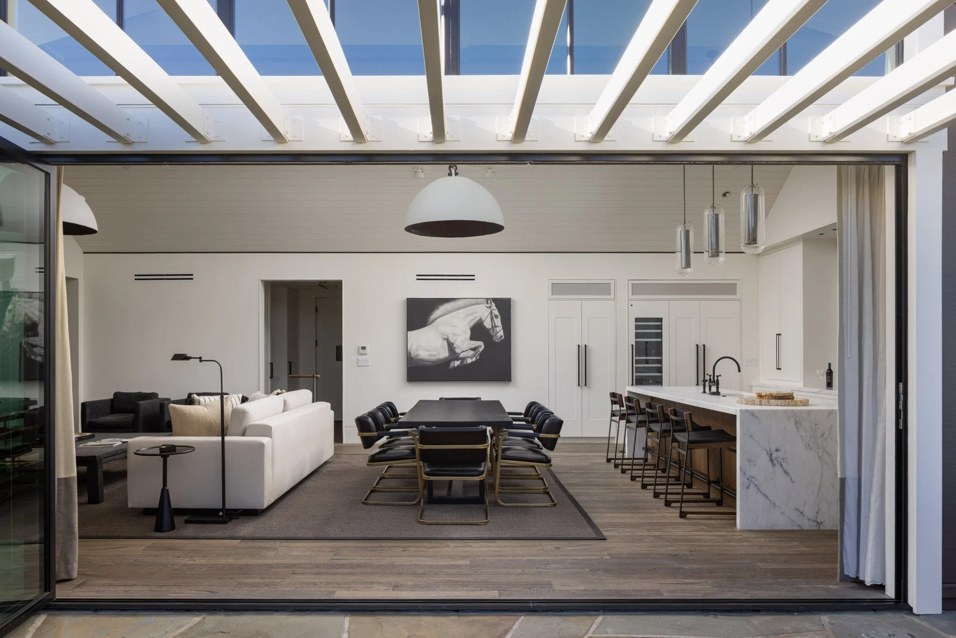Open-concept living and dining area with a modern kitchen, black and white furniture, and a painting of a jumping horse on the wall.