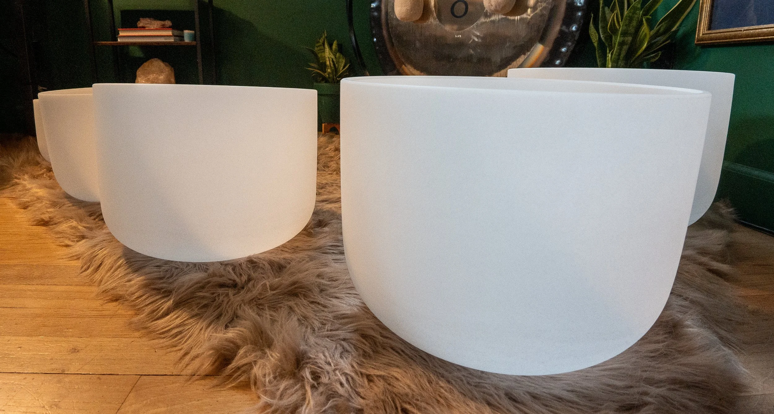 White crystal singing bowls arranged on a soft rug in a sound bath setup, with a gong visible in the background.