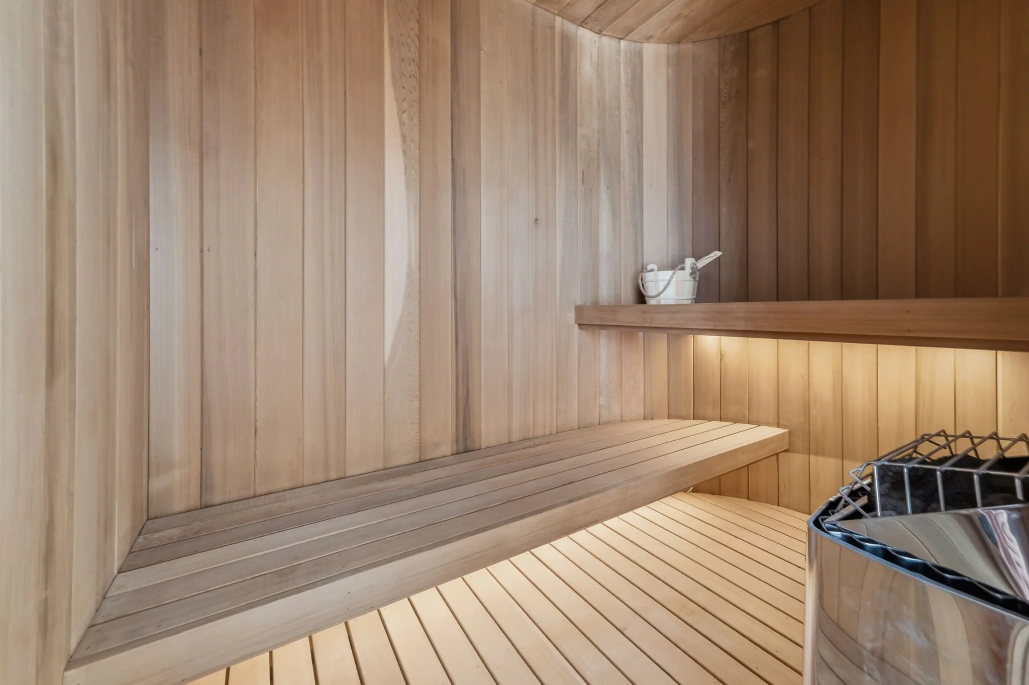 Empty wooden sauna room with a bench, a bucket with a ladle, and a heater with stones.