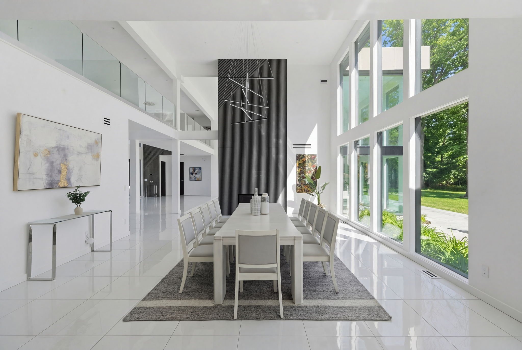 Modern dining room with large windows, white furniture, and black accents, overlooking a green outdoor area.