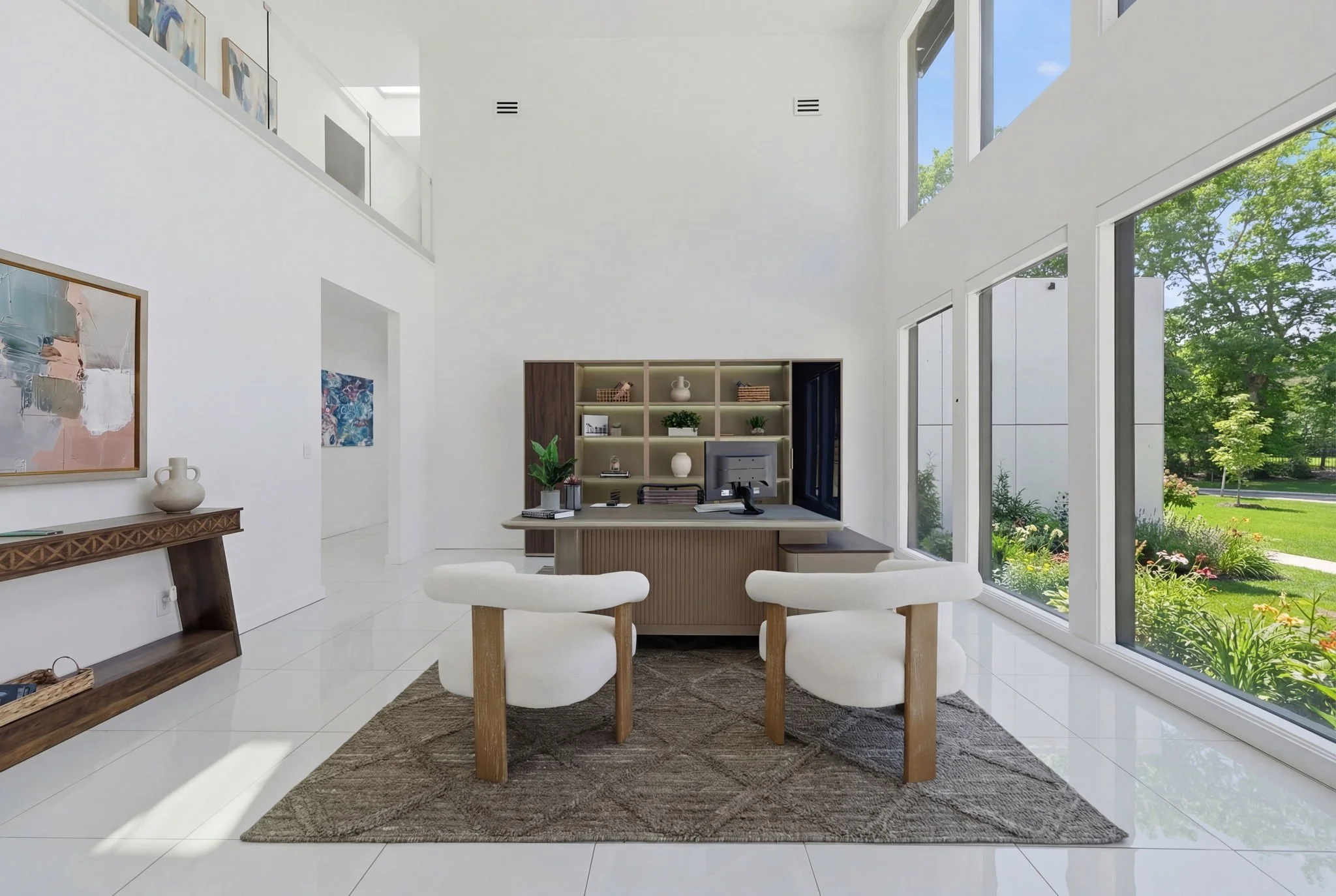 Modern office with a curved desk, two white chairs, a dark wood and beige bookcase, large windows with a garden view, and white walls.