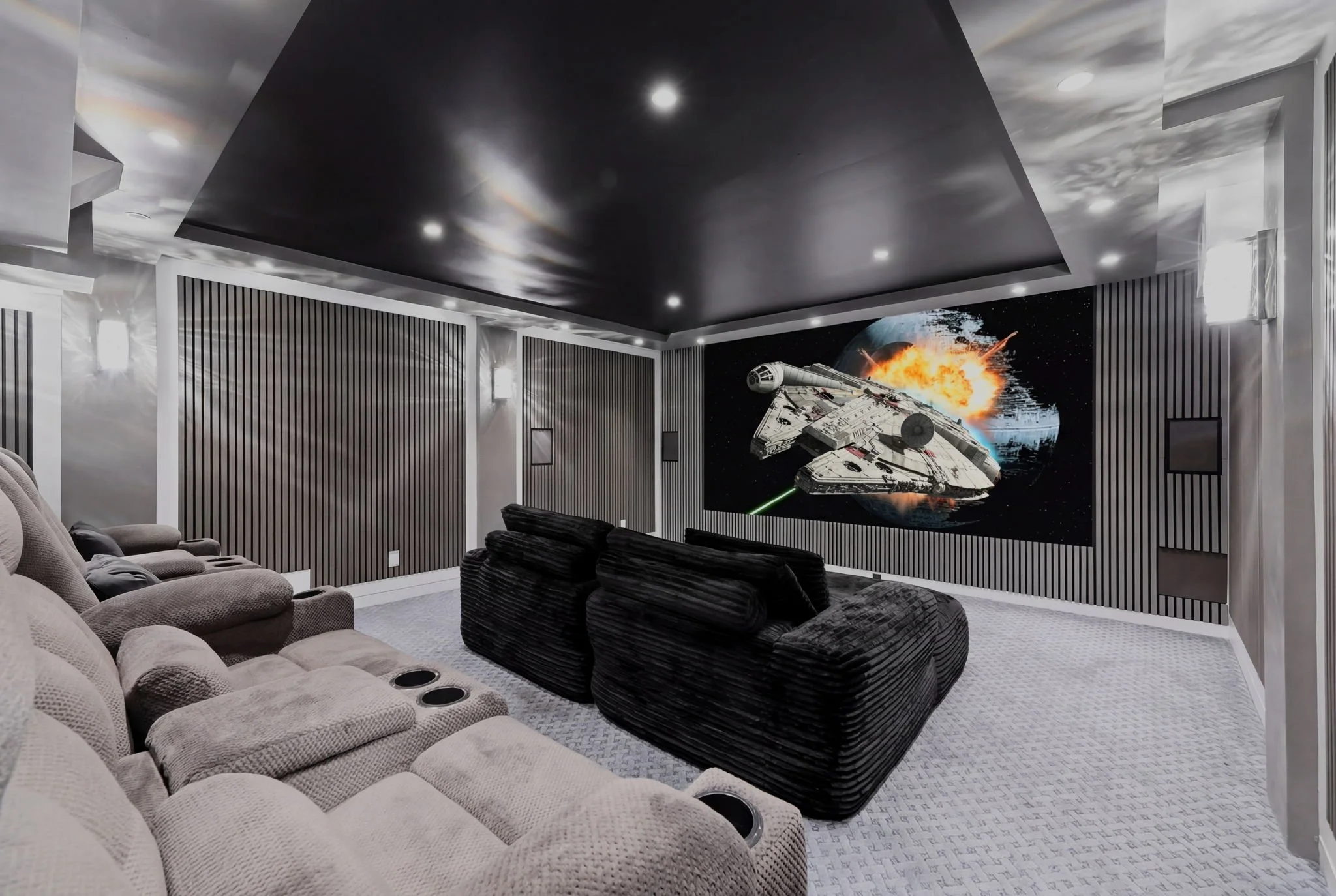 Home theater with a large screen showing a spaceship in space, plush beige and black recliner seats, and black acoustic wall panels, with ceiling and wall lights.
