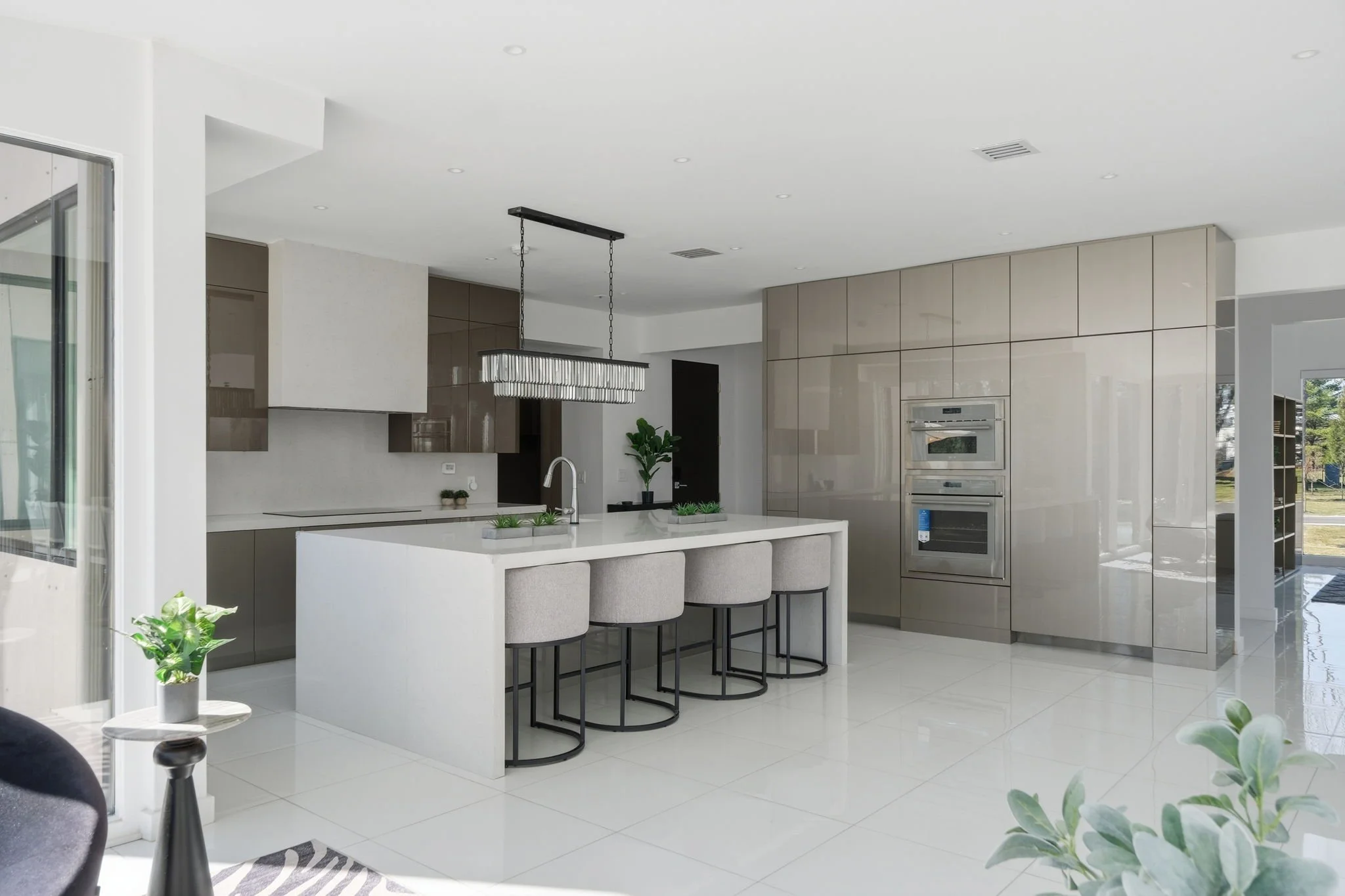 Modern kitchen with white island, beige and gray cabinets, built-in double oven, and hanging light fixture.