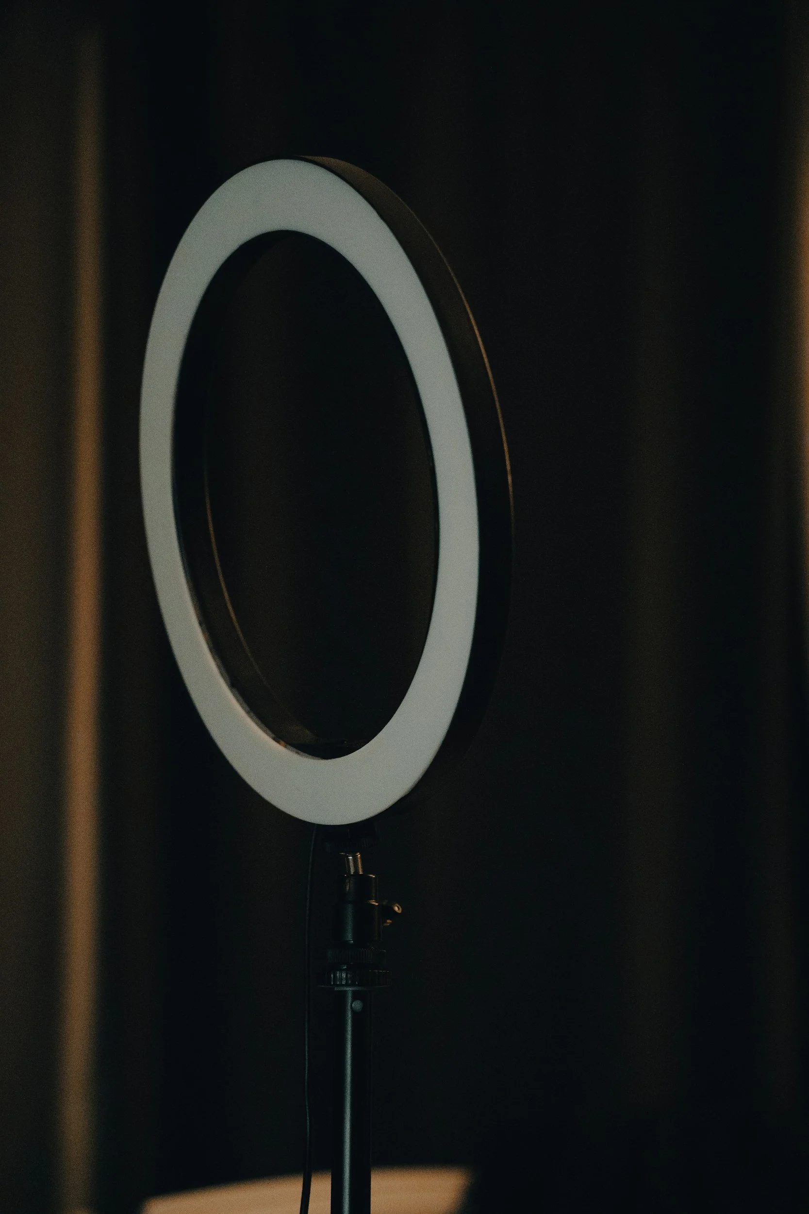 A speaker with a white ring in a dark room, set up on a stand with a cable hanging down.