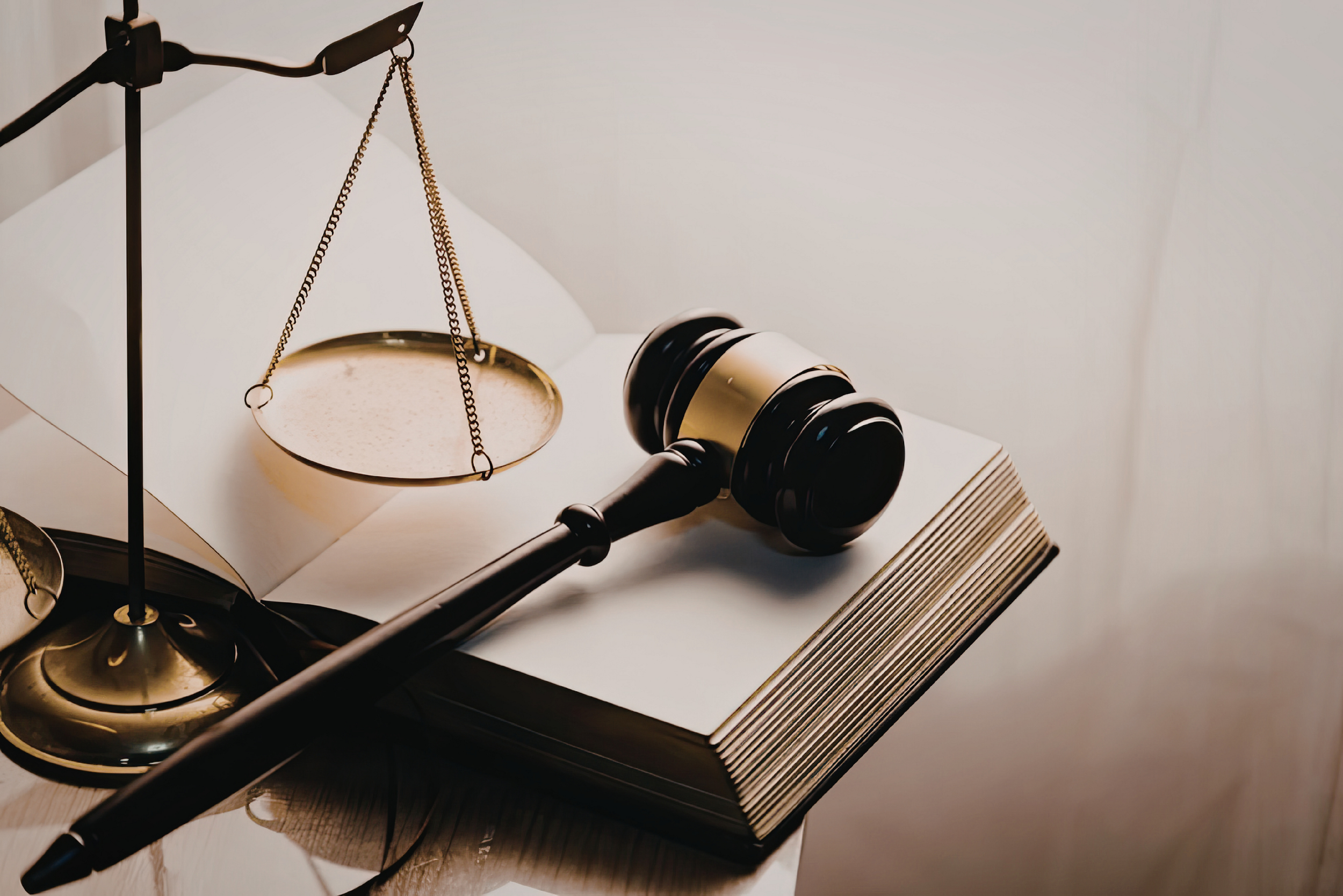 A gavel, a set of scales, an open law book, and a folder are arranged on a desk.