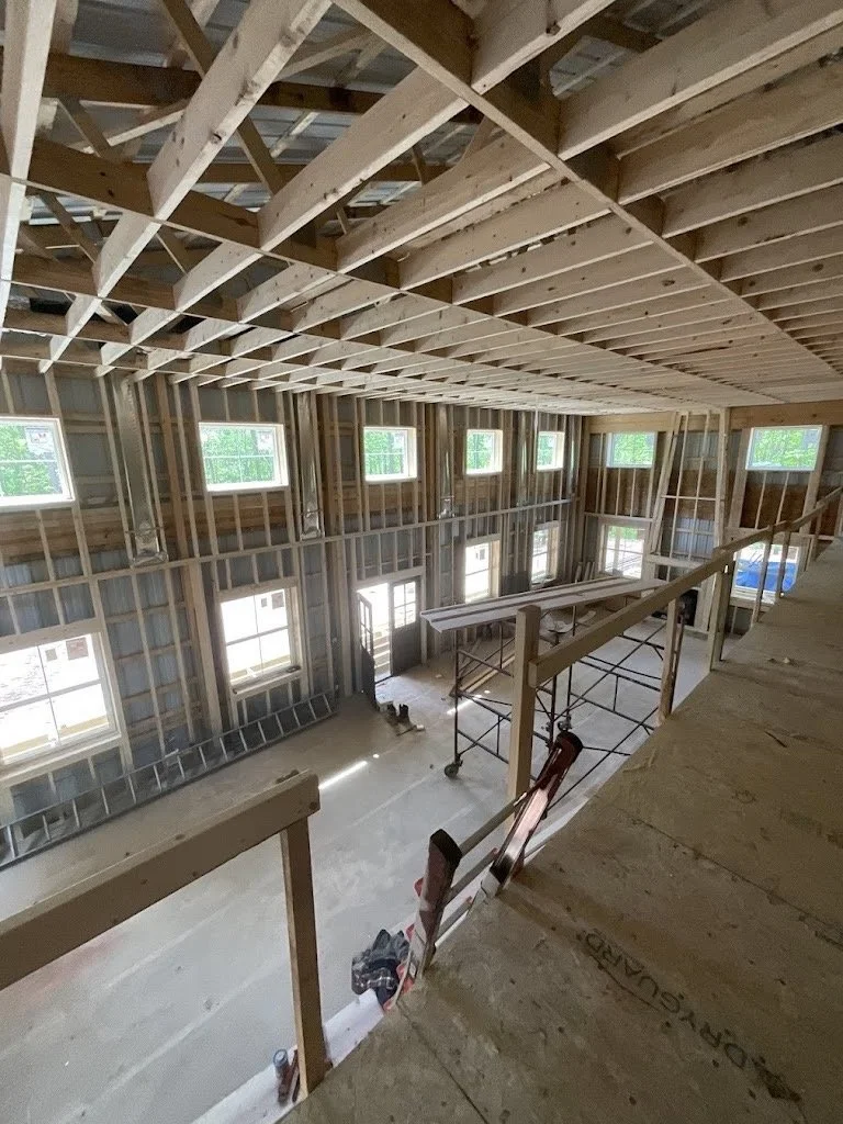 Interior view of a building under construction with exposed wooden framework, multiple windows, and scaffolding.