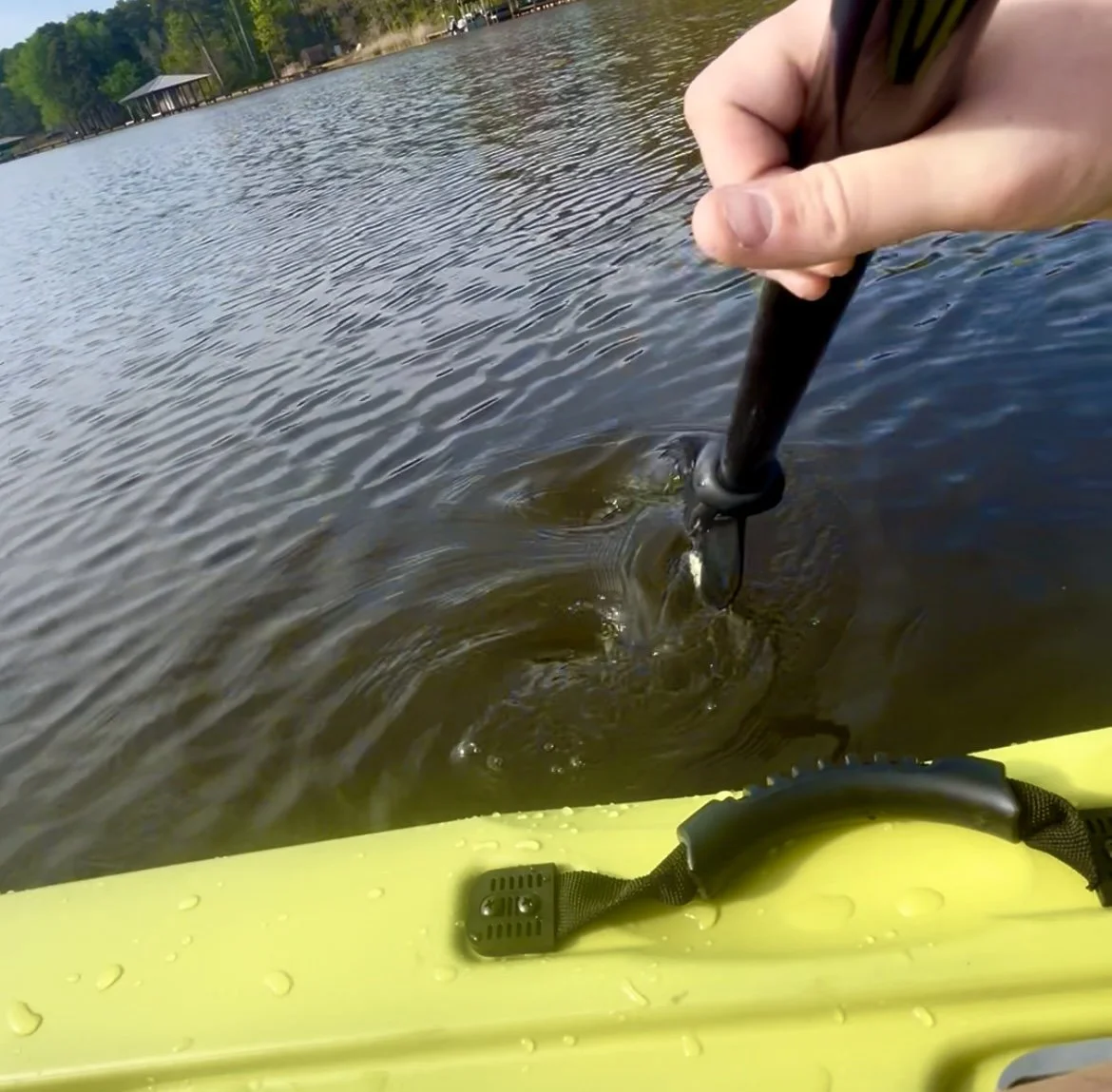 A person holding a paddle in a yellow kayak on a lake with a paddle in the water
