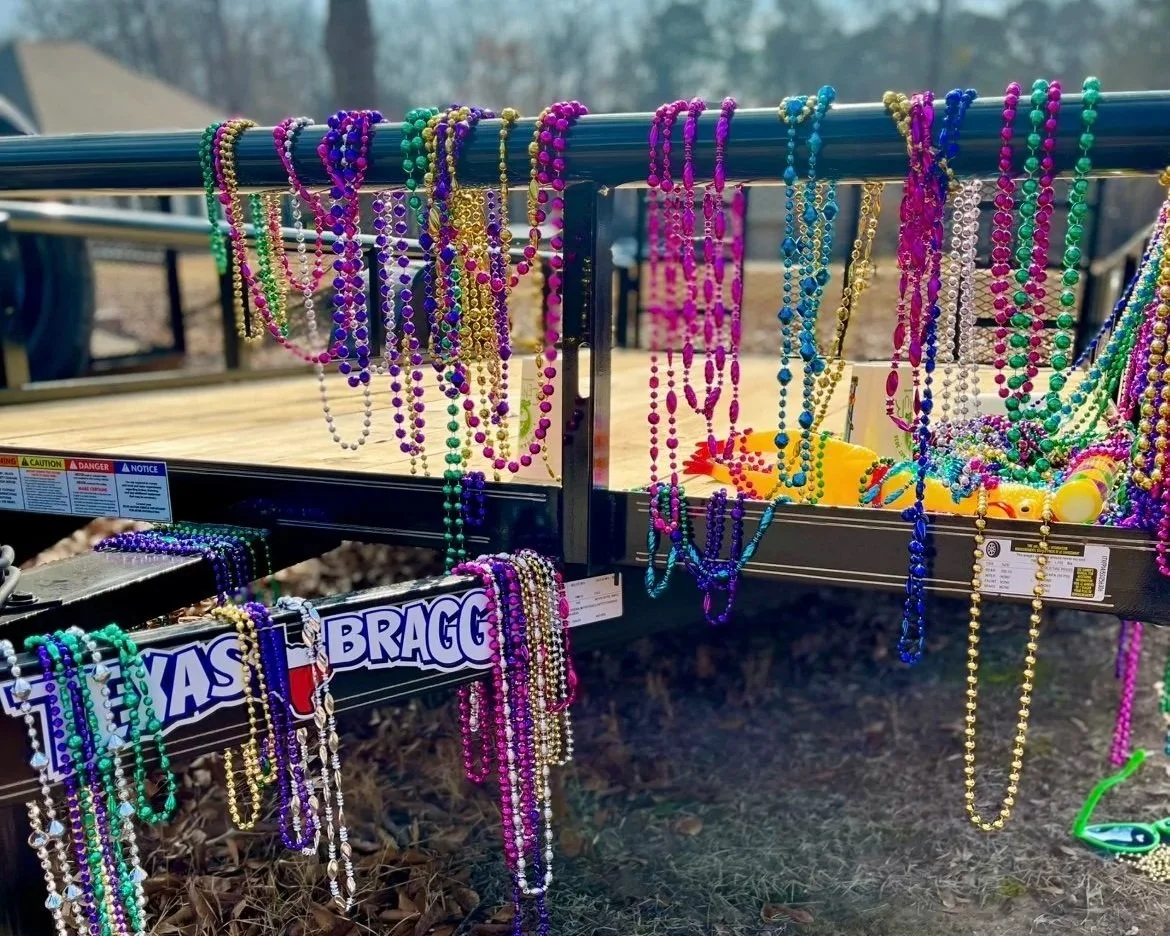 Colorful Mardi Gras bead necklaces hanging from a trailer railing outdoors.