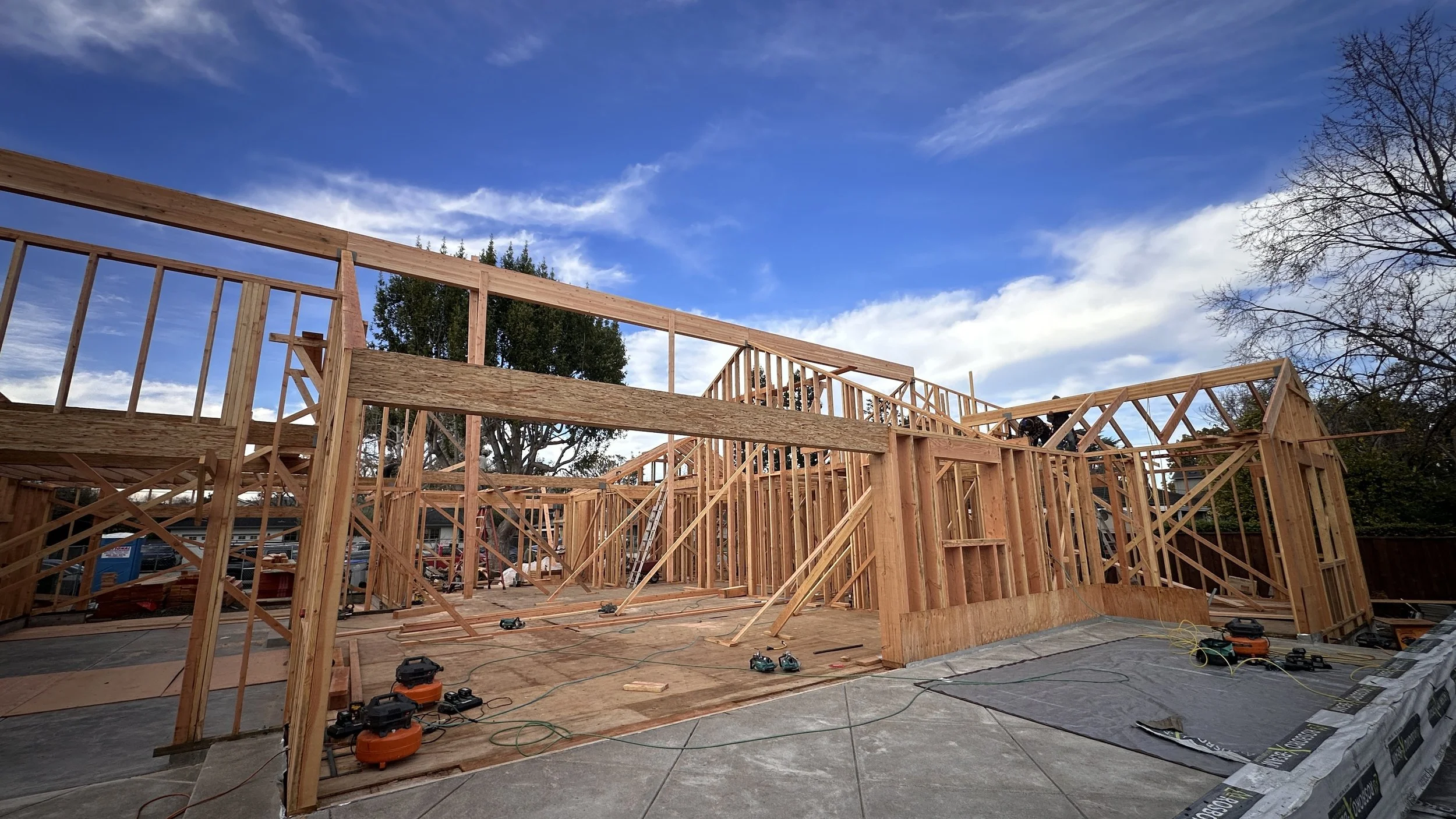 Wood framing structure of a house under construction with blue sky and some clouds above.
