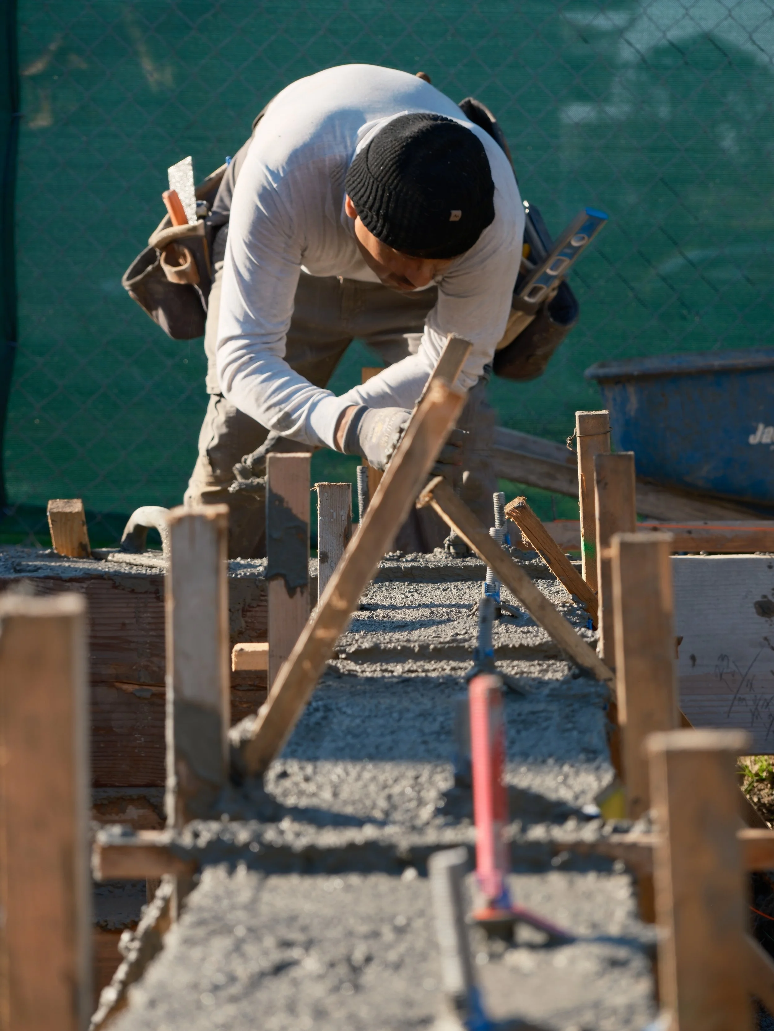 Construction worker pouring concrete into a wooden form for a sidewalk or foundation.