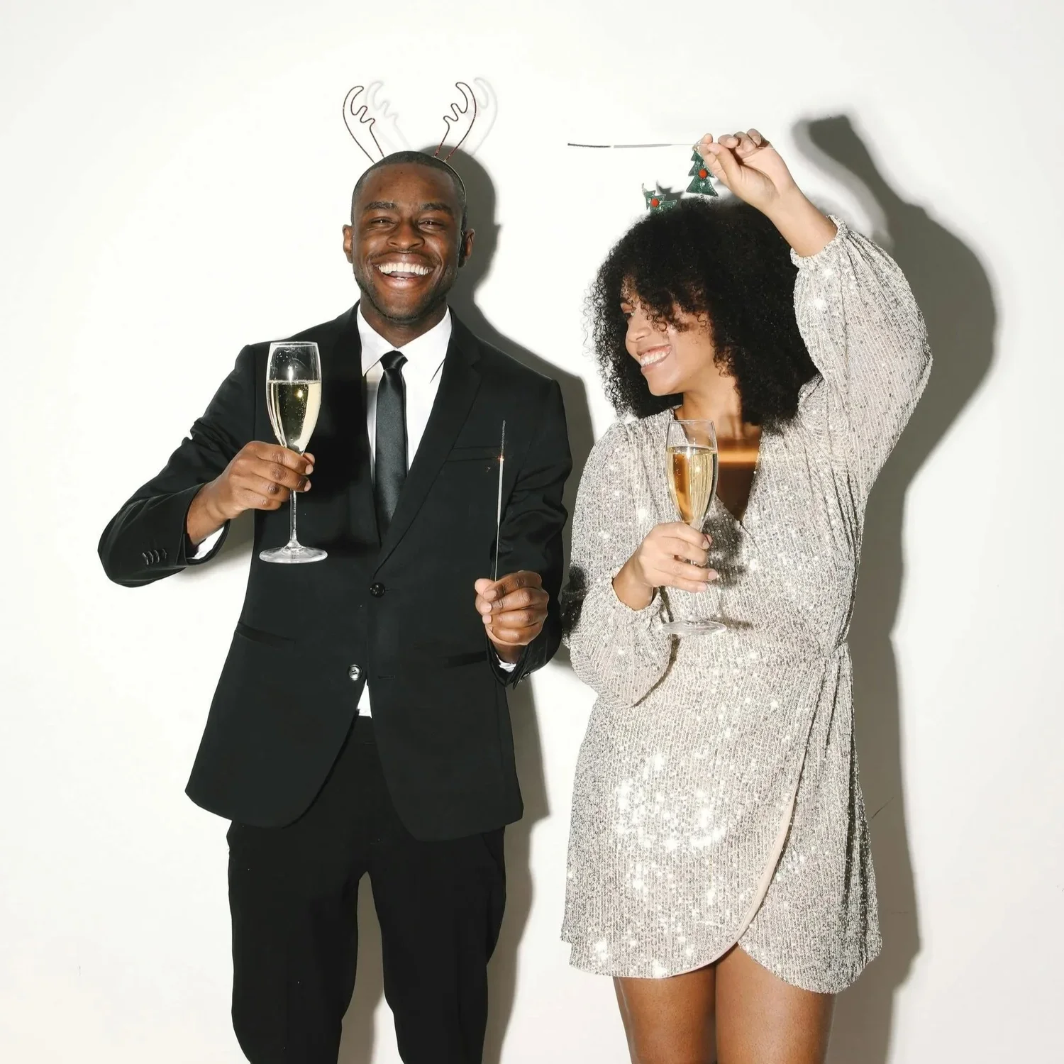Man and woman pose for a photo while holding champagne flights and sparklers.