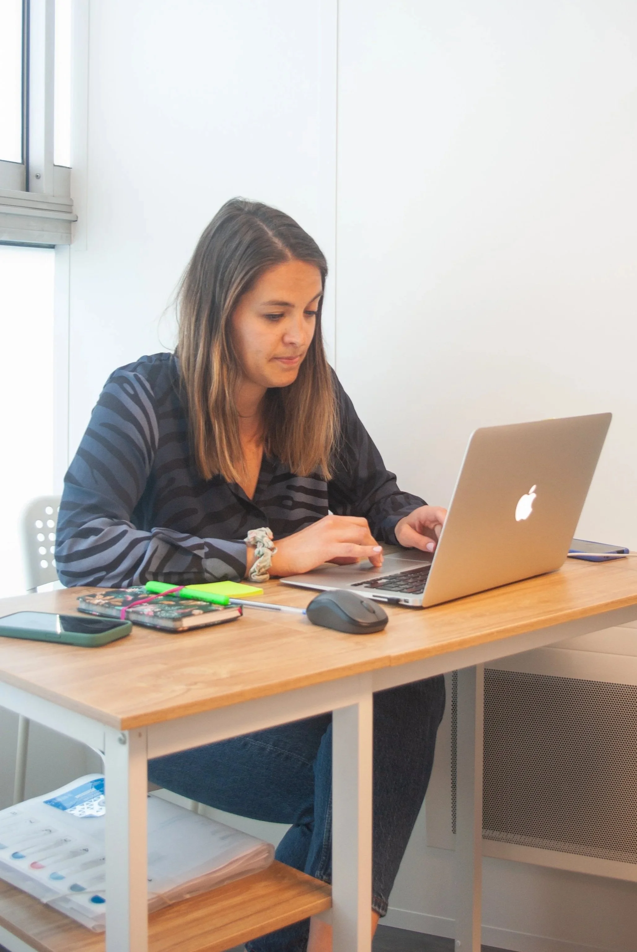 Une femme assise à un bureau, utilisant un ordinateur portable, dans un environnement de bureau lumineux.